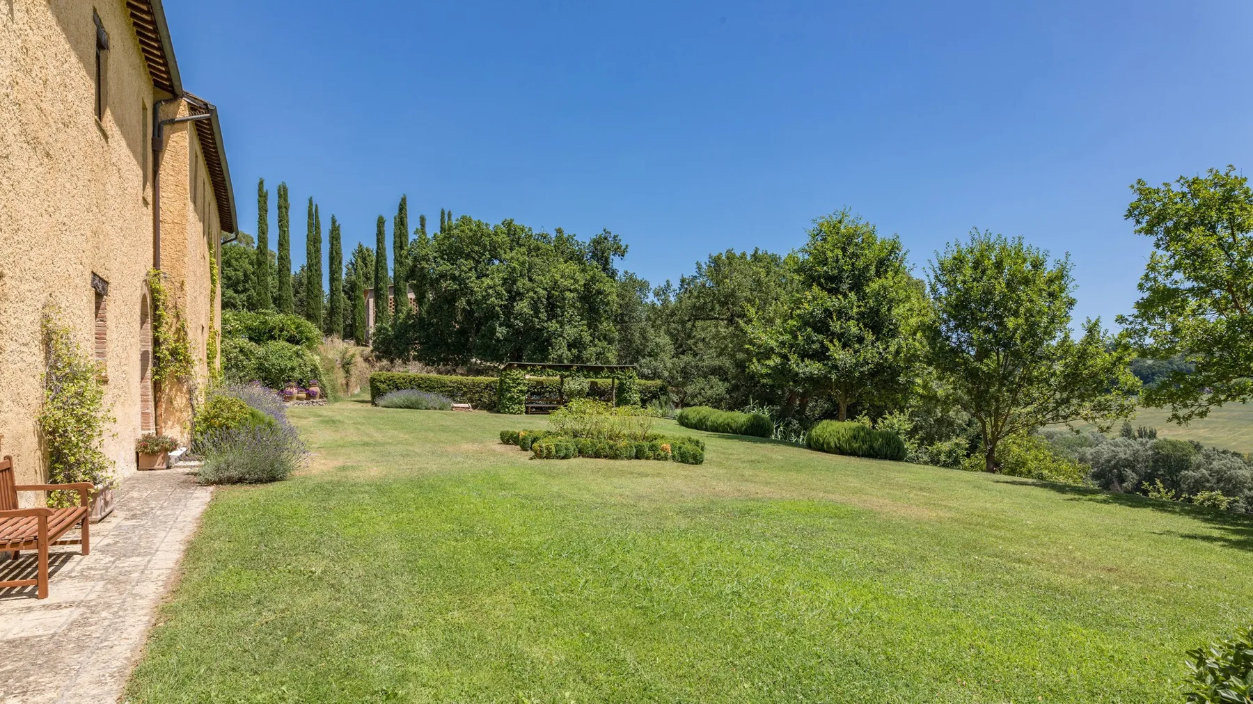 A broad lawn beside a stone building, with trees and garden beds in the background.