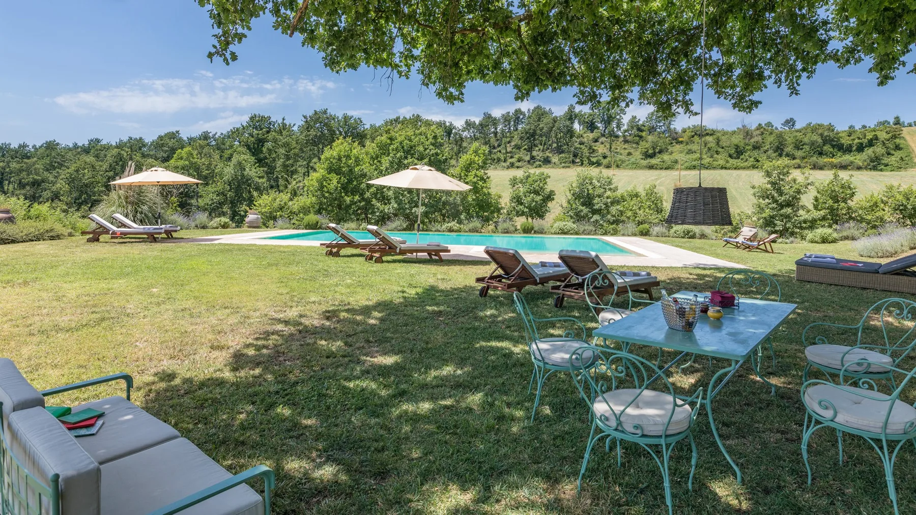 An outdoor pool area has lounge seating, umbrellas, and a shaded dining table.