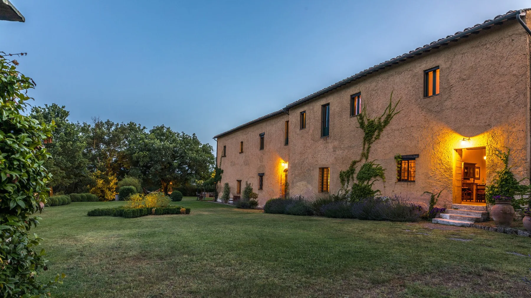 A long stone building stands beside a landscaped lawn and garden.