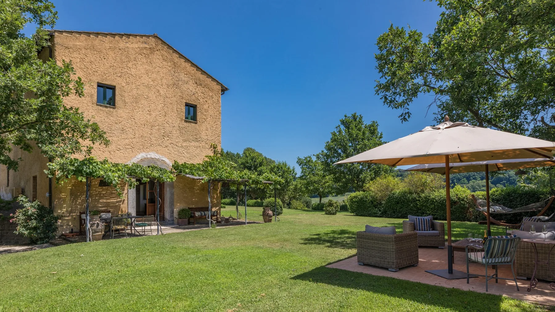 A sunny garden patio with outdoor seating beside a rustic building.