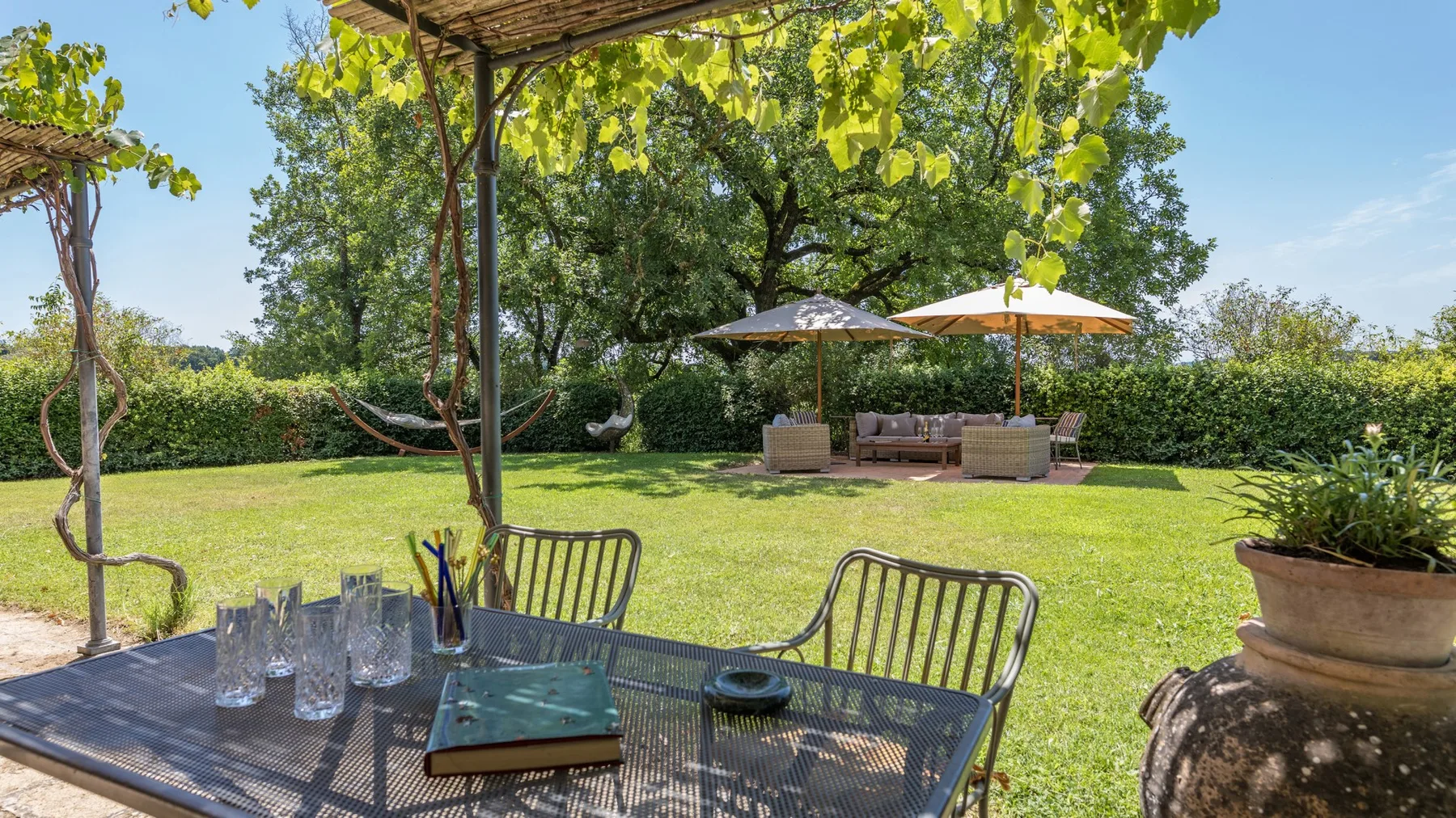 A garden patio with outdoor seating beneath a canopy, overlooking a green lawn.