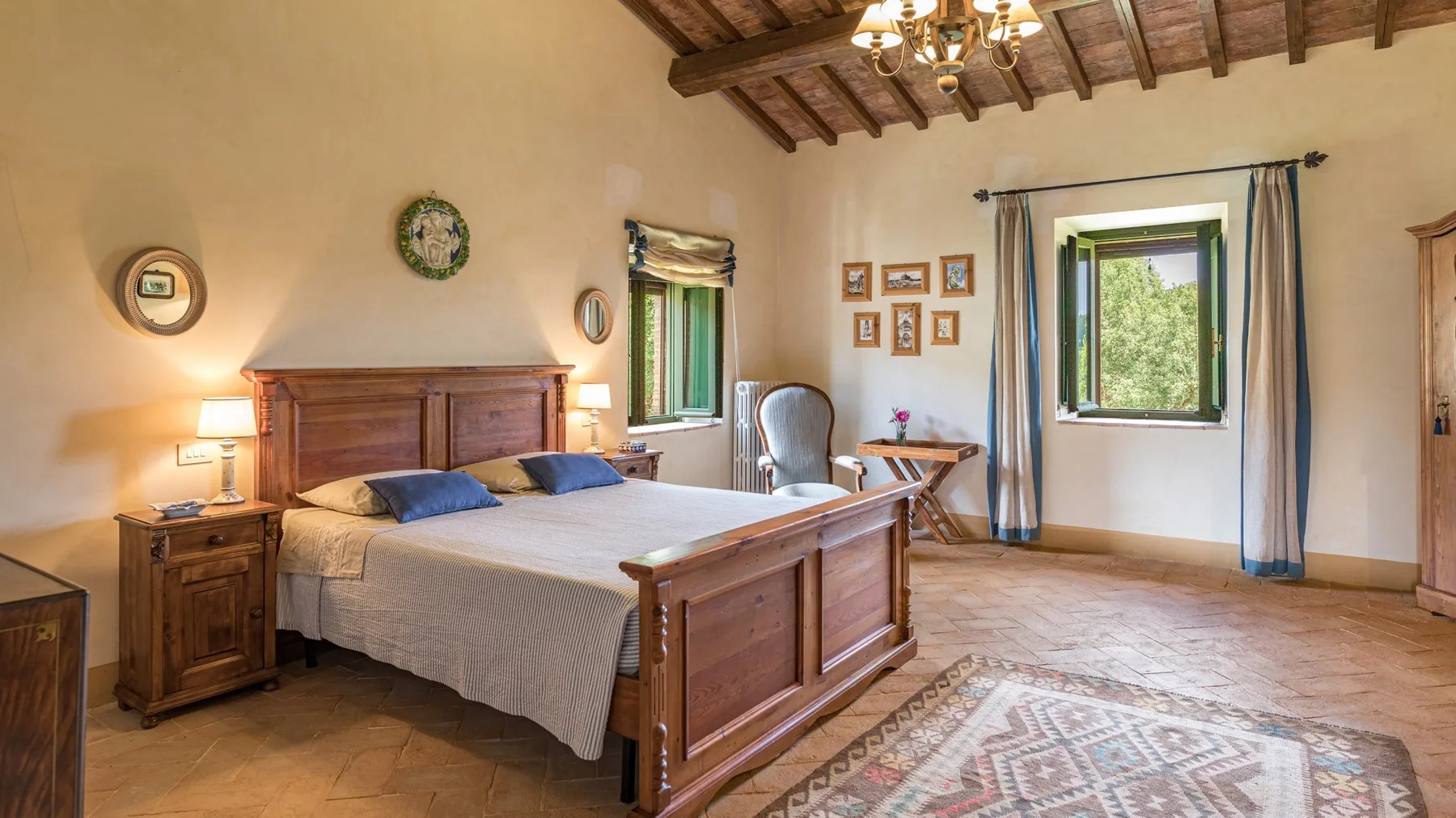 A bedroom with a wooden bed, bedside tables, and windows overlooking greenery.