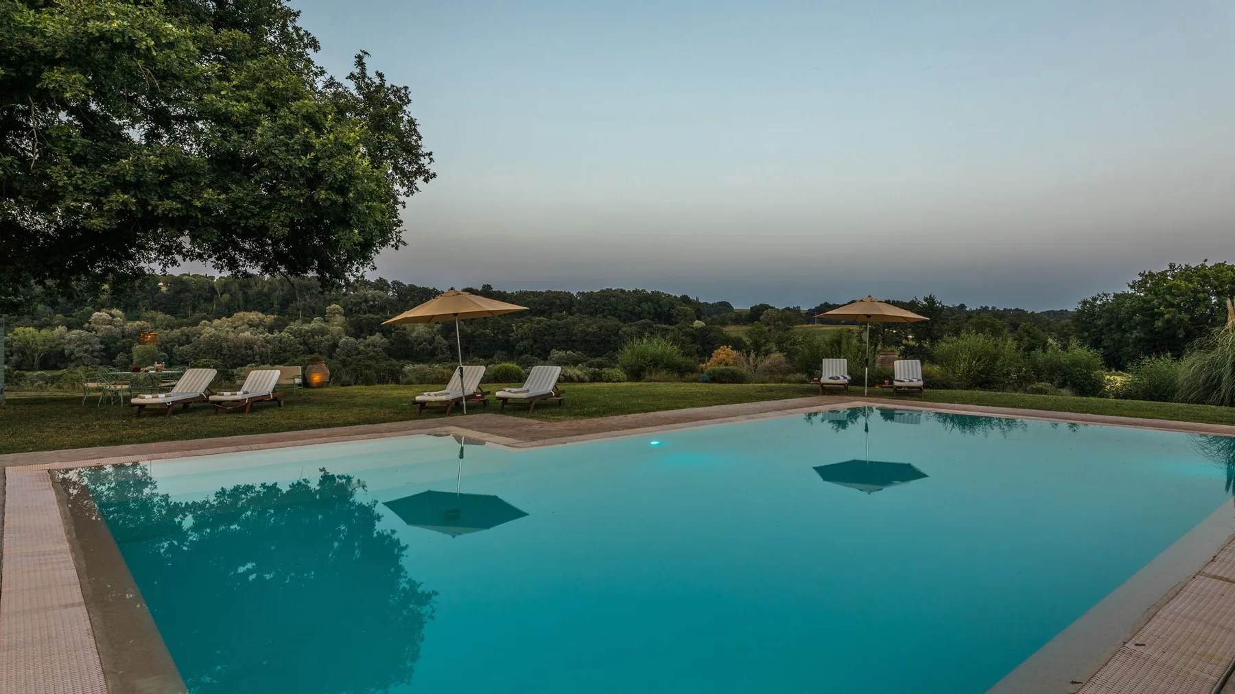 An outdoor swimming pool overlooks a tree-covered landscape, with sun loungers along the edge.