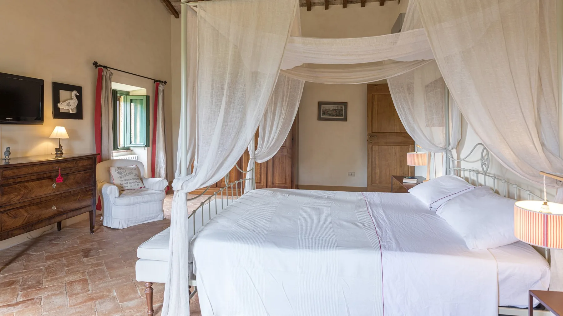 A bedroom with a white canopy bed and a wooden dresser.