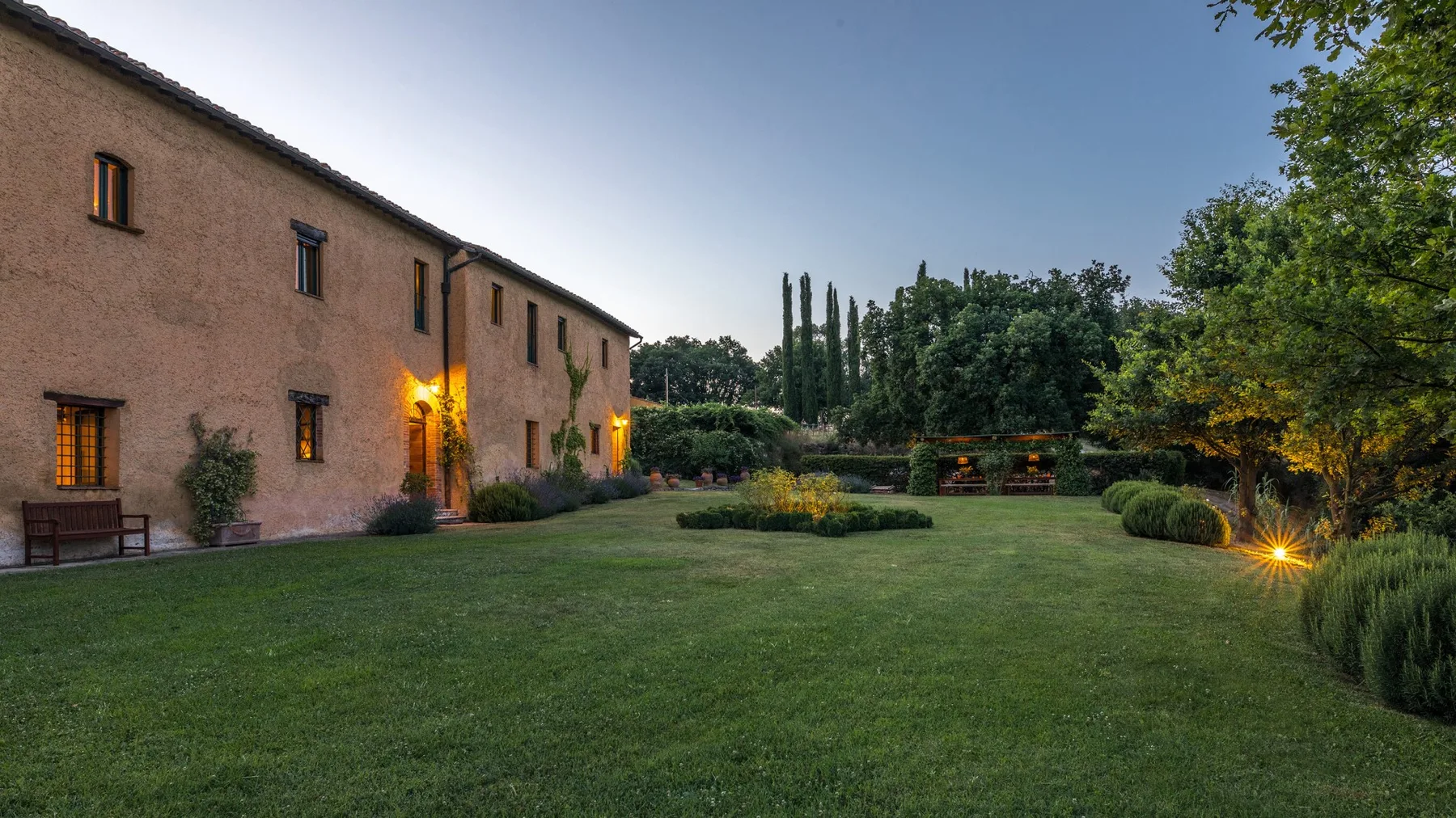 A landscaped garden lawn beside a long building, with trees and shrubs.