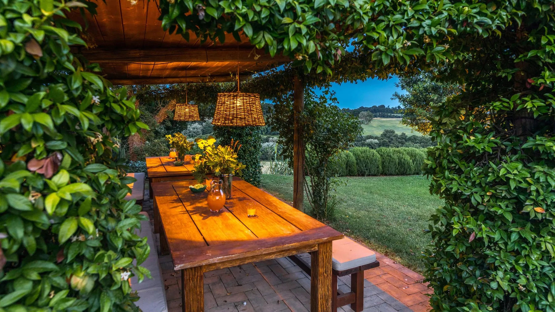 A covered outdoor dining table opens onto a grassy landscape.