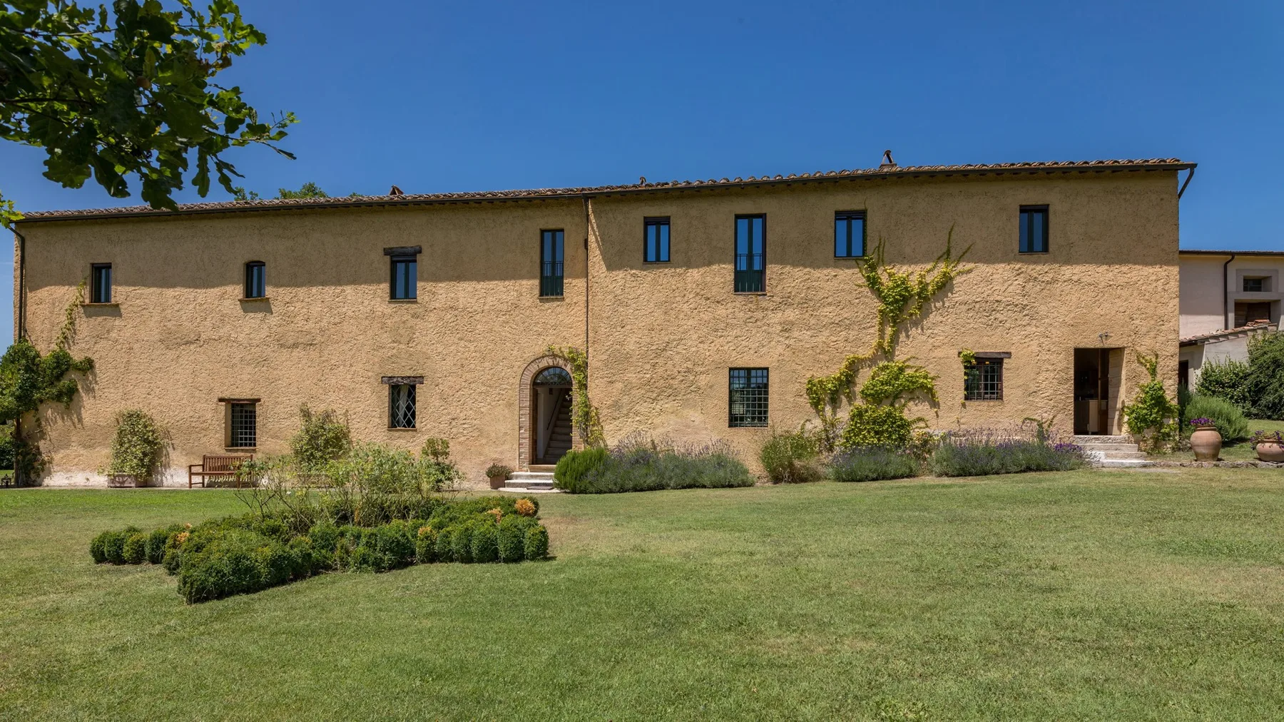 A long stone-colored building stands behind a broad green lawn and garden.