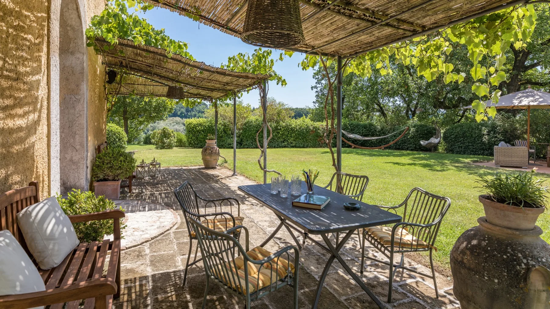 A shaded patio with outdoor seating overlooks a green garden.