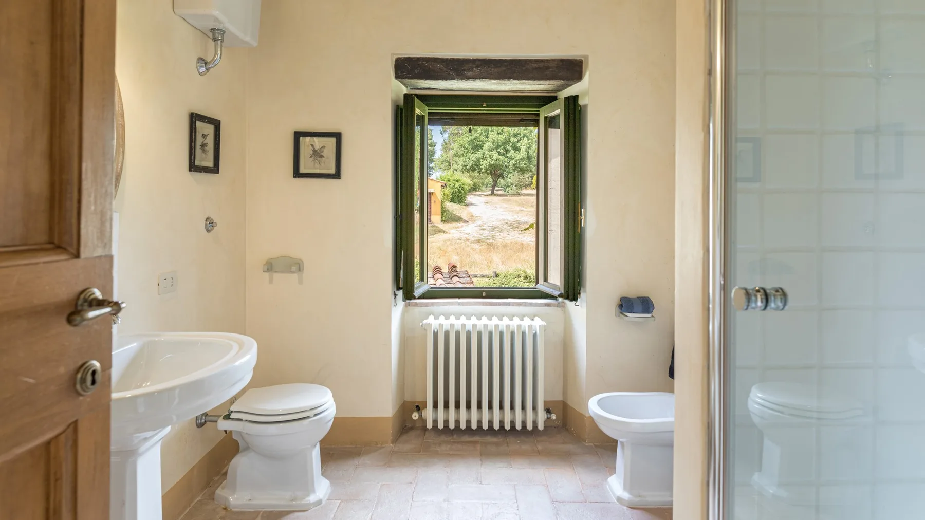 A bathroom with a window overlooking greenery and a radiator beneath it.