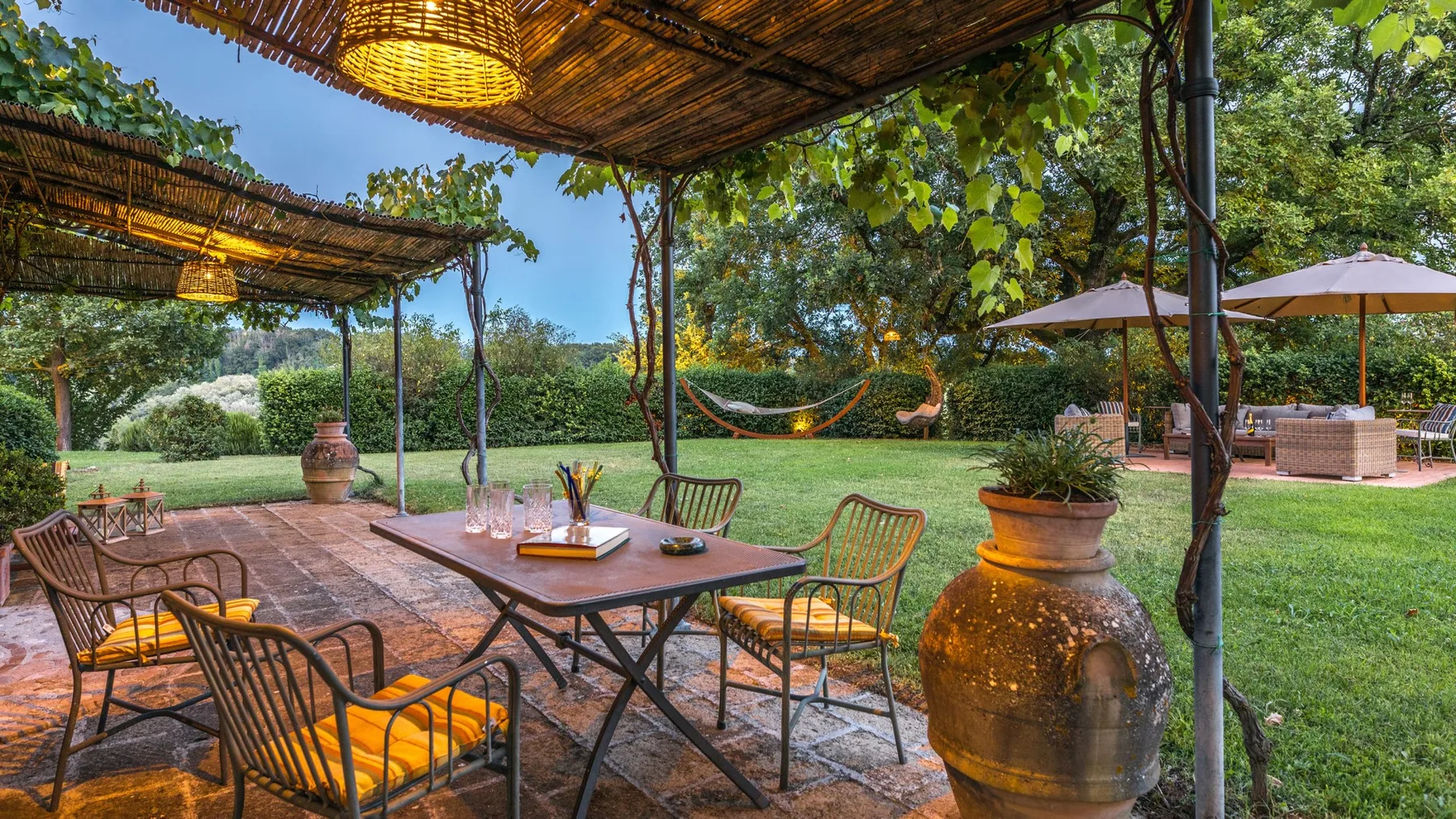 A garden patio with an outdoor dining table, seating, and leafy greenery.