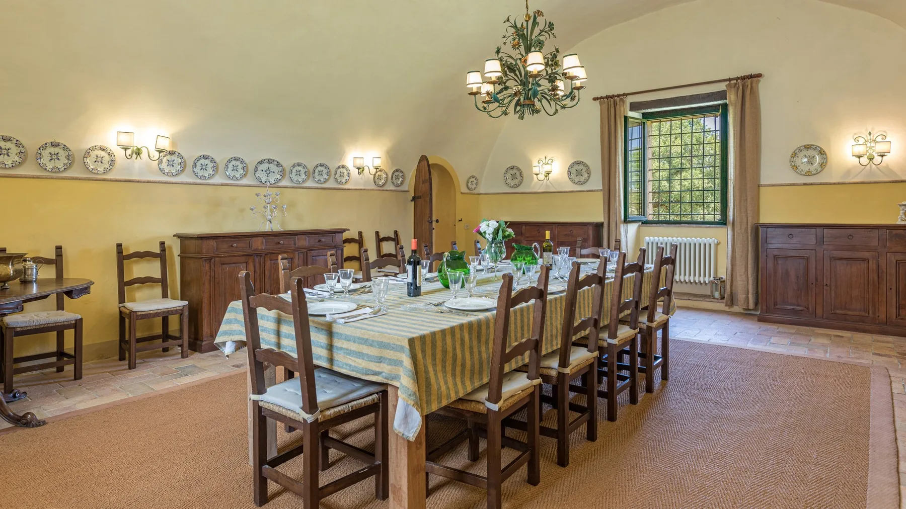 A dining room with a long table set with dishes and wooden chairs.