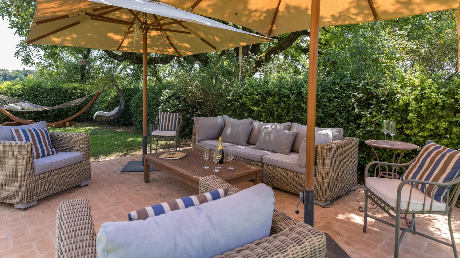 An outdoor patio seating area beneath large umbrellas, surrounded by leafy greenery.