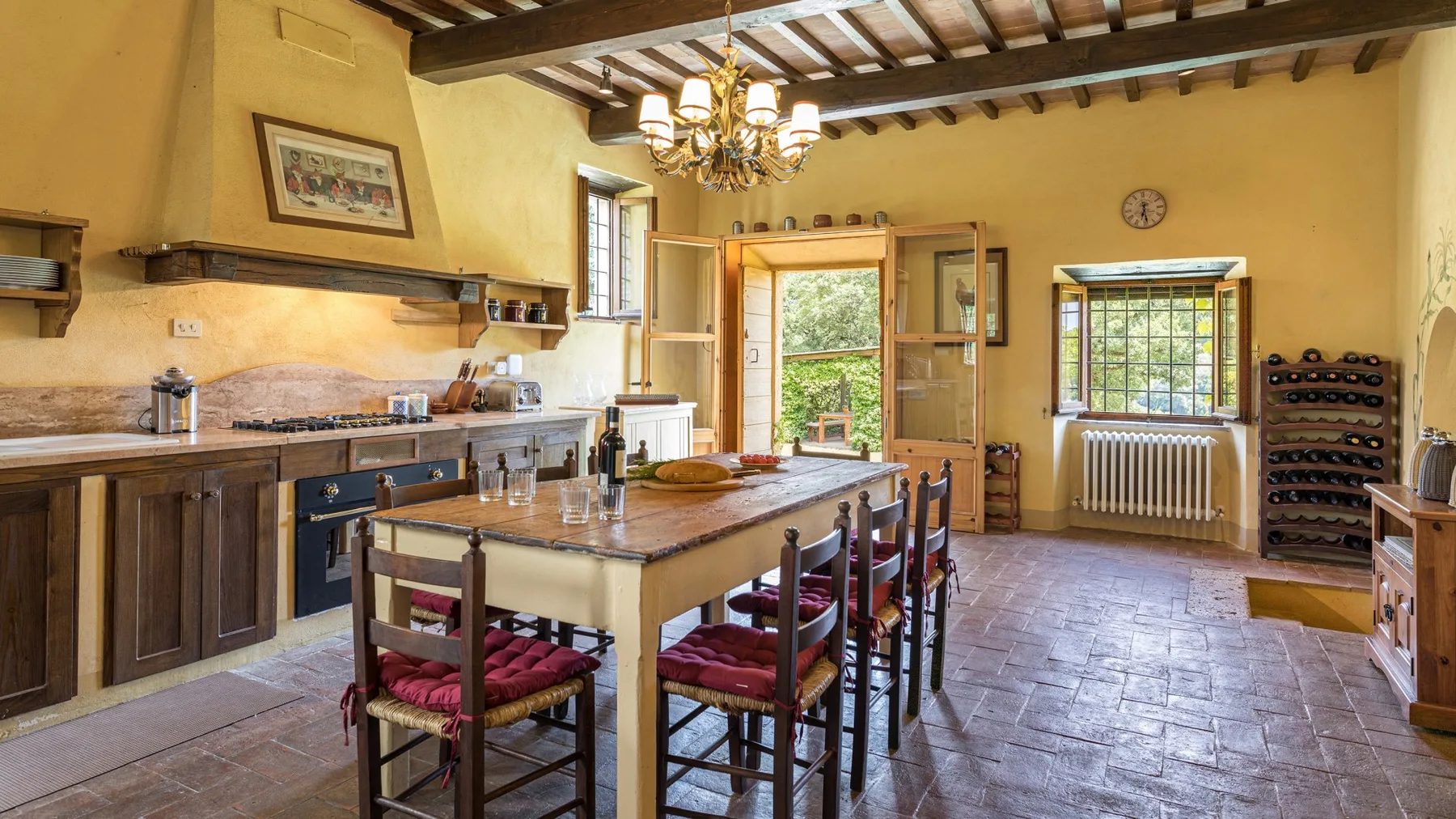 A rustic kitchen with a central dining table beneath exposed wooden ceiling beams.