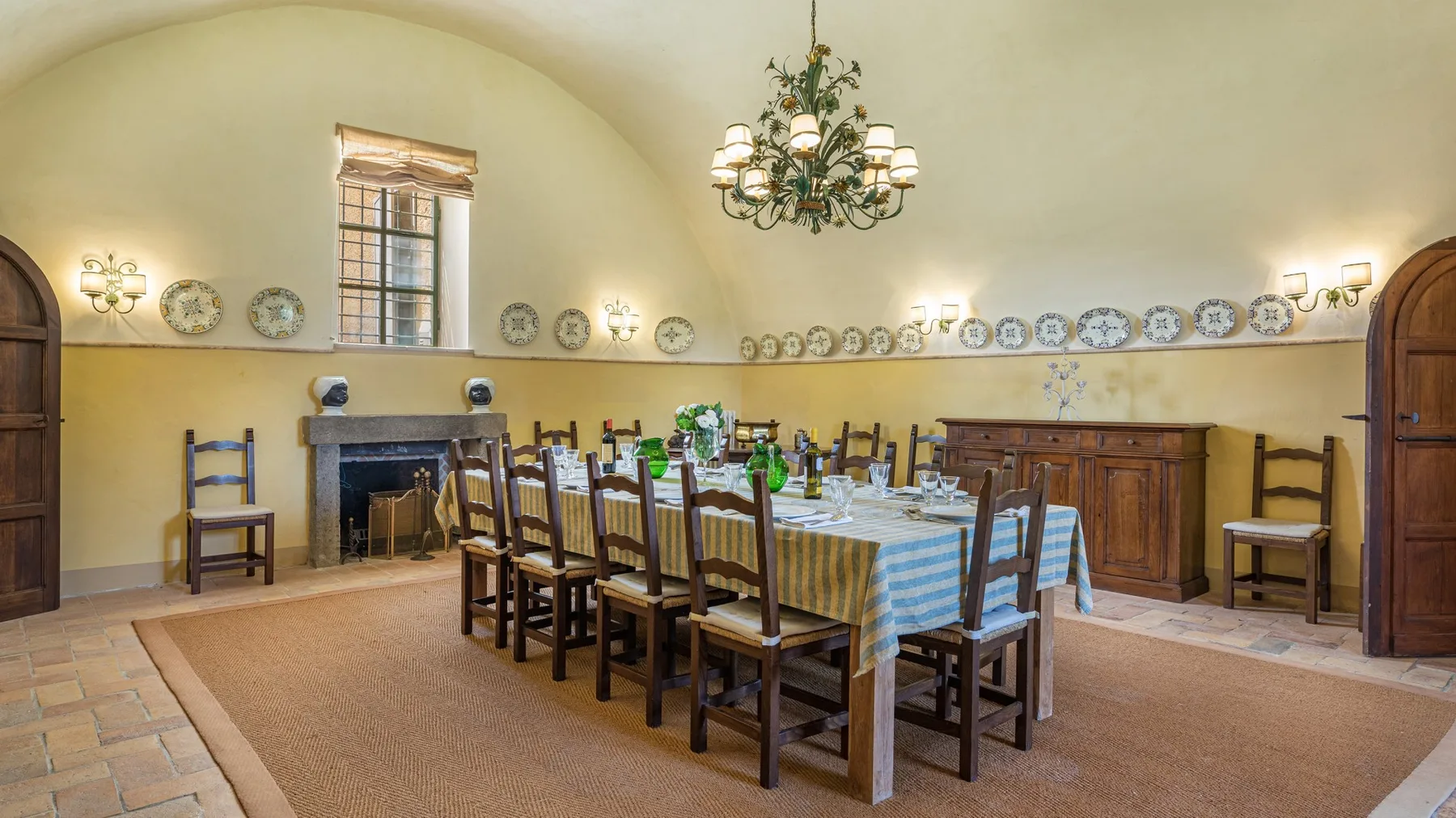 A dining room with a long table set for a meal beneath a chandelier.