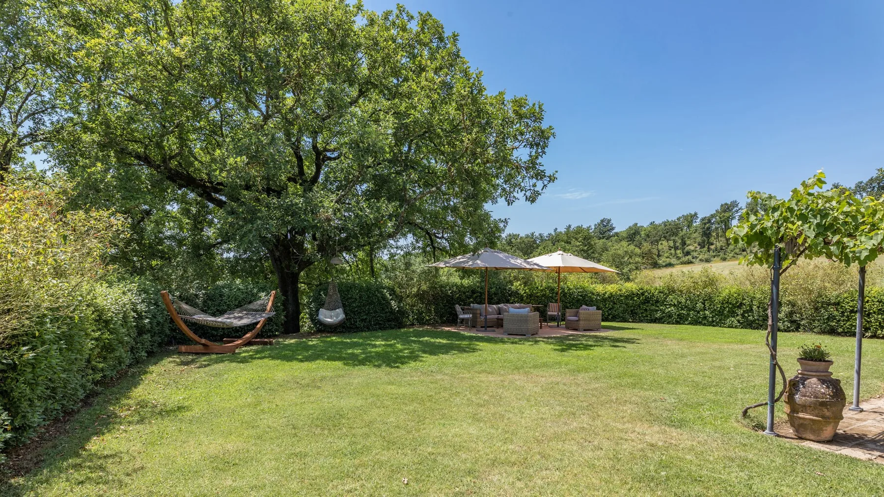 A garden lawn sits beneath a large leafy tree, with shaded seating nearby.