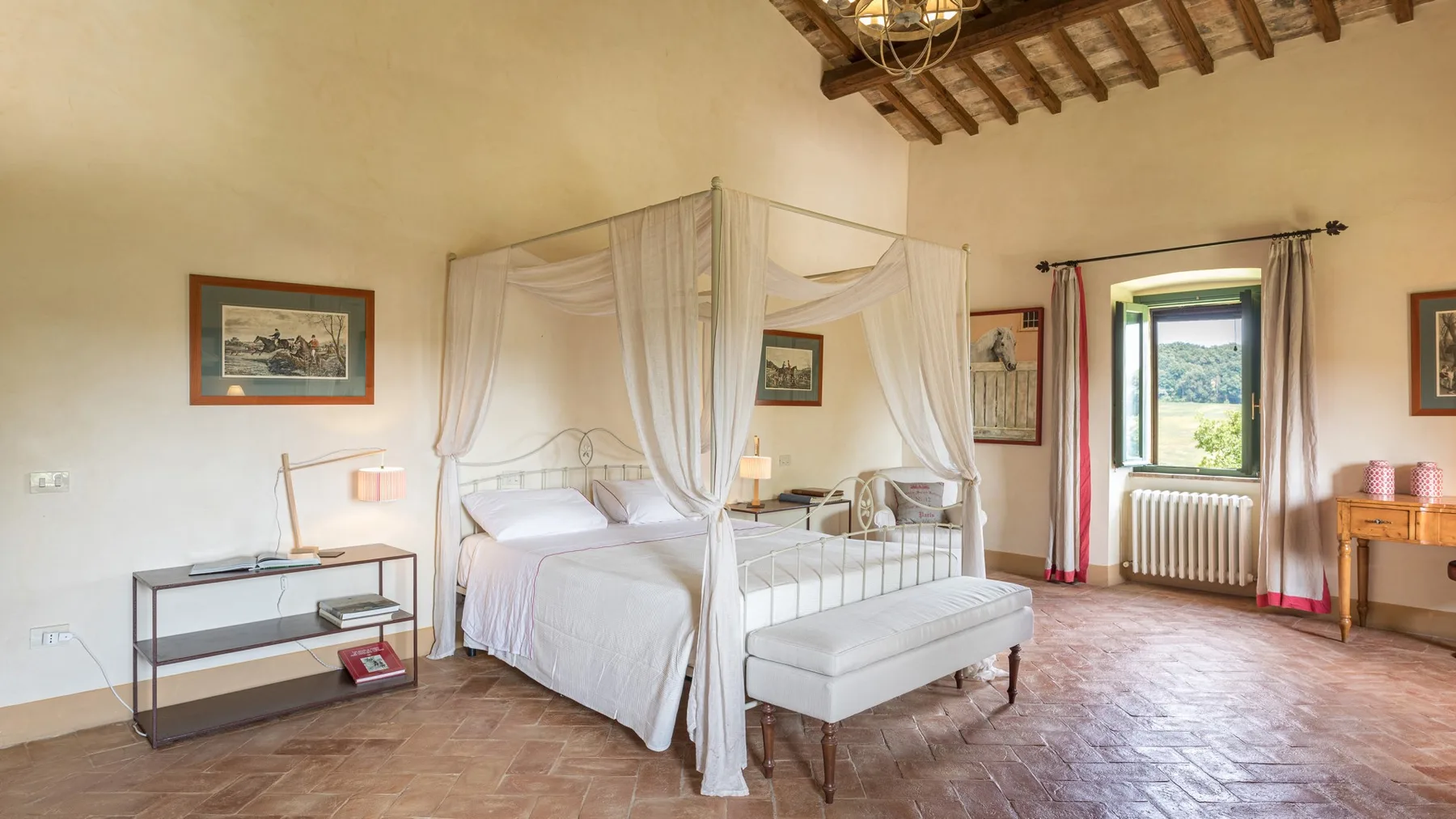 A bedroom with canopy beds, a bench, and a window overlooking greenery.