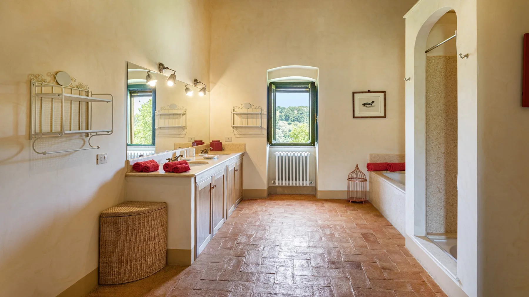 A bright bathroom with a long vanity, two windows, and a bathtub.