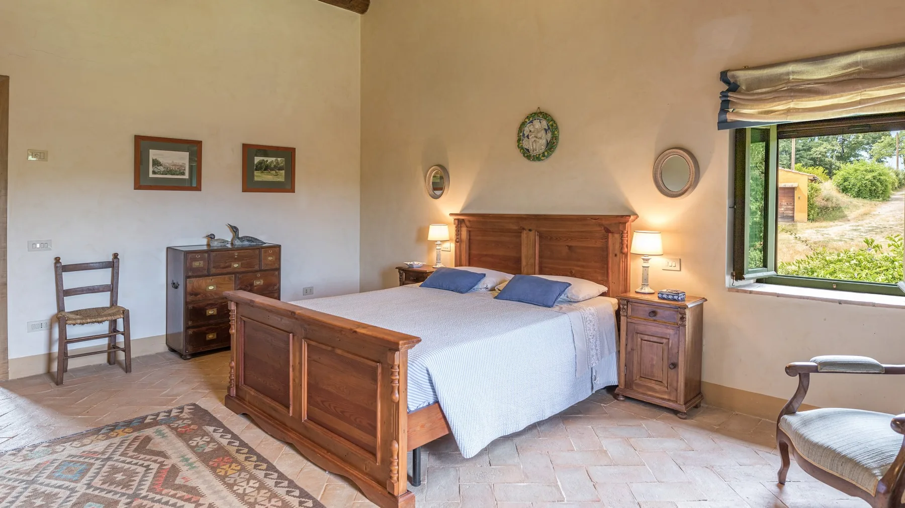 A bedroom with a wooden bed, bedside tables, and a window overlooking greenery.