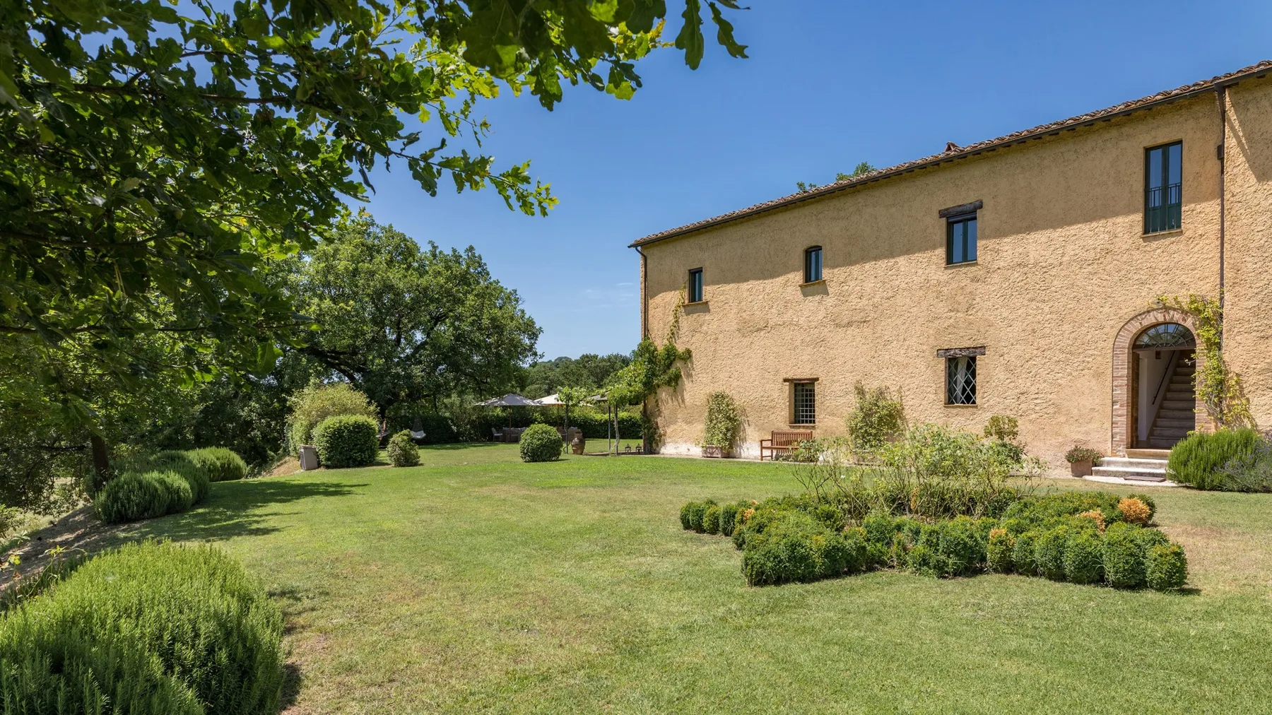A stone house stands beside a broad green lawn and landscaped garden.
