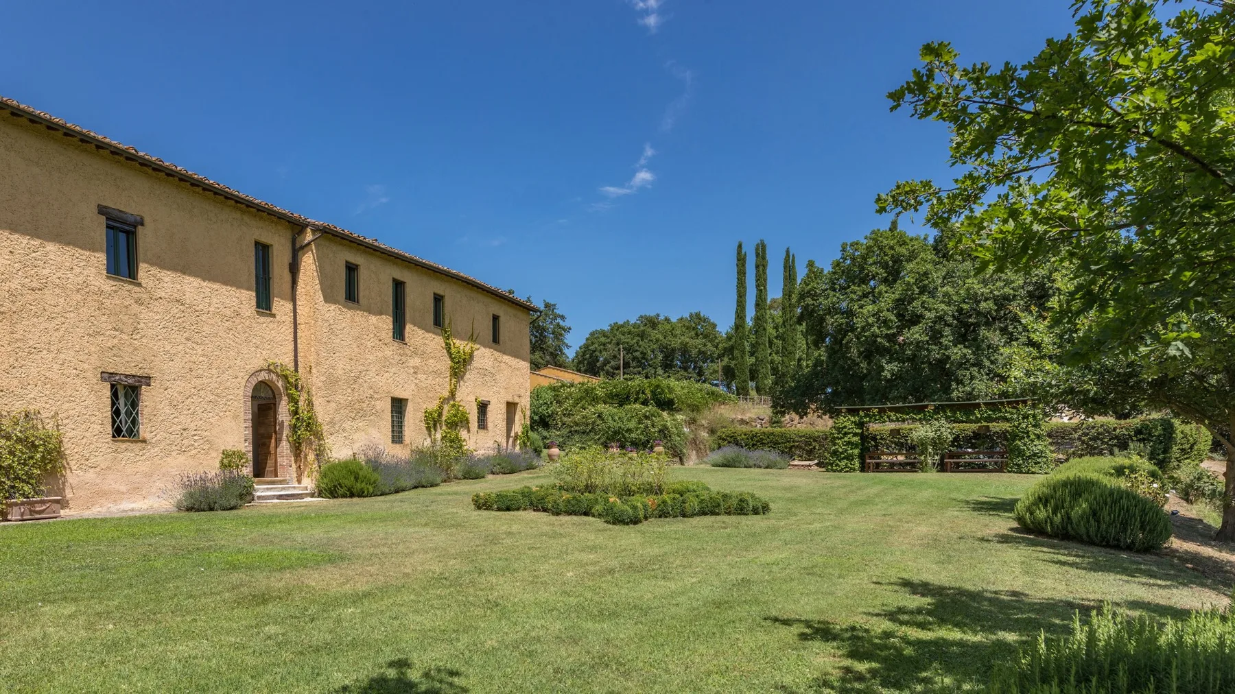 A landscaped garden lawn stretches beside a long stone building and leafy trees.