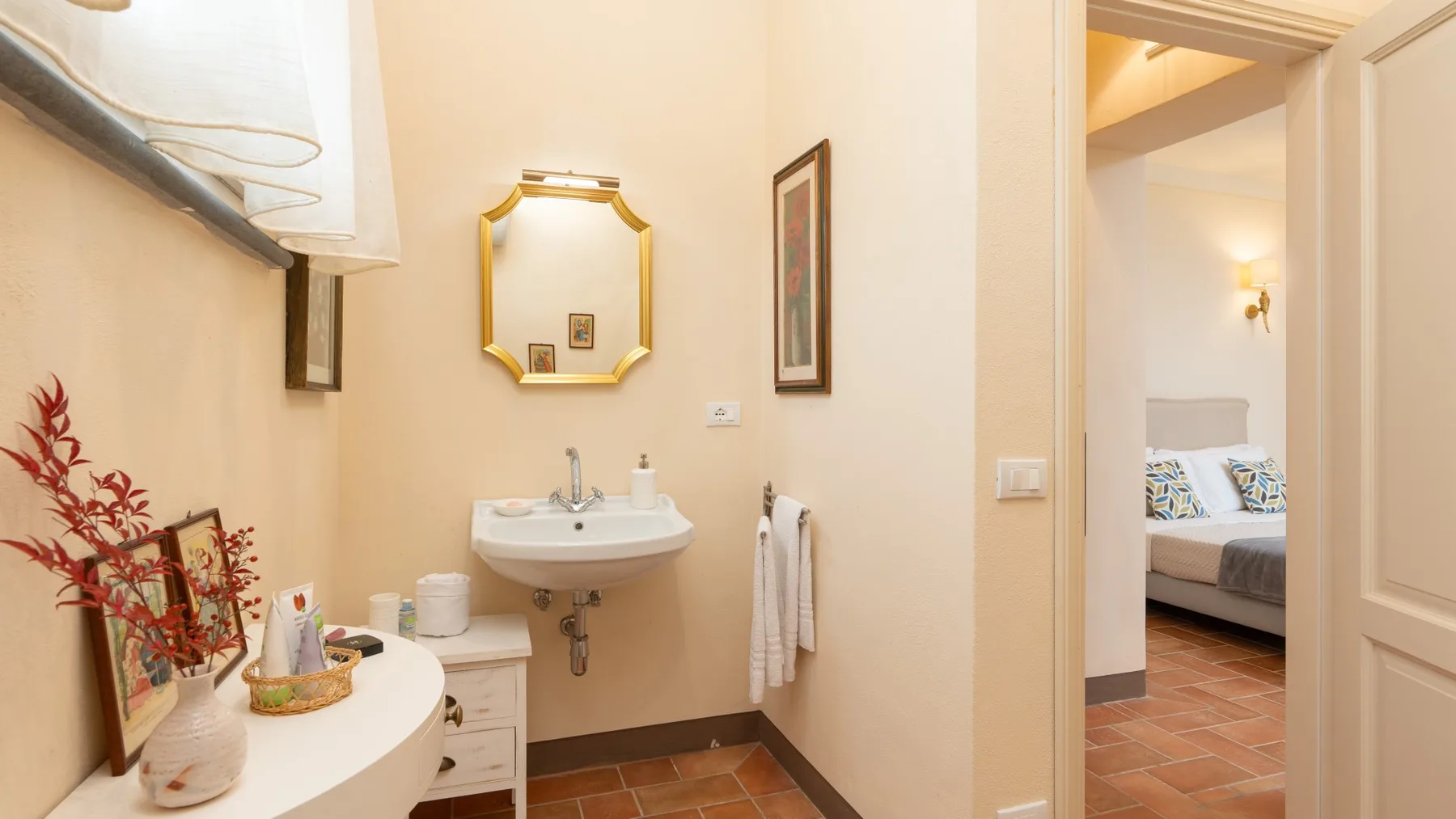 Un baño con lavabo y espejo junto a una puerta abierta que da a un dormitorio.