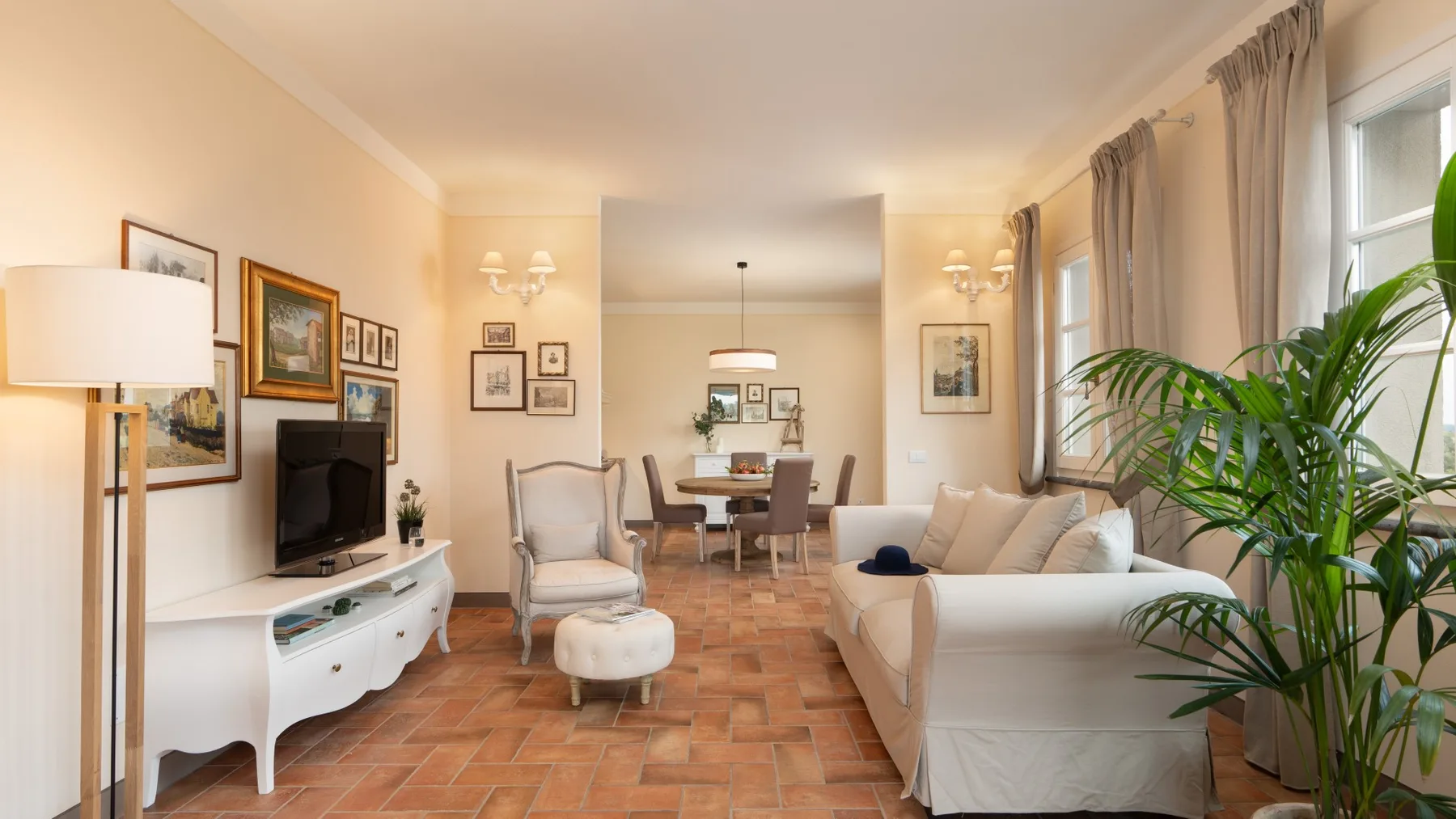 Una sala luminosa con asientos, un televisor y un comedor al fondo.
