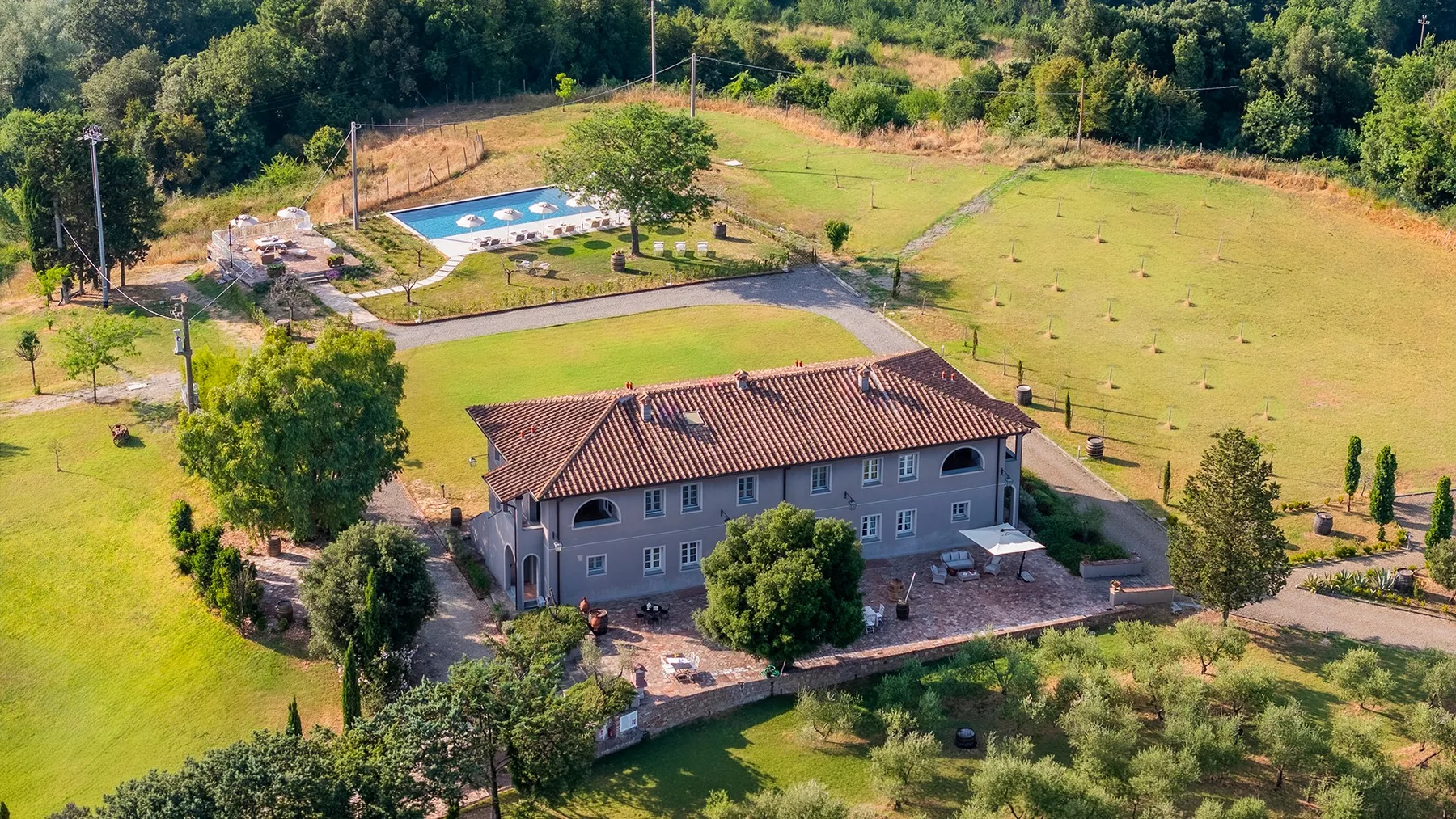 Una casa grande está rodeada de césped abierto, árboles y una piscina.