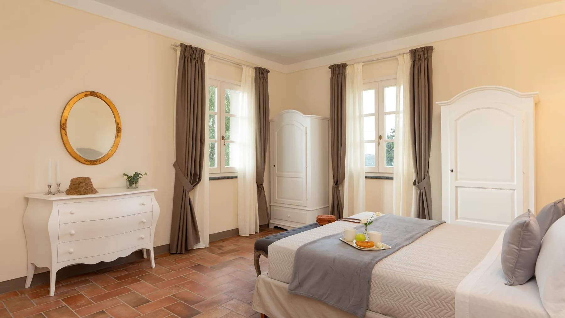 Un dormitorio con una cama bien arreglada, dos armarios blancos y ventanas con cortinas.
