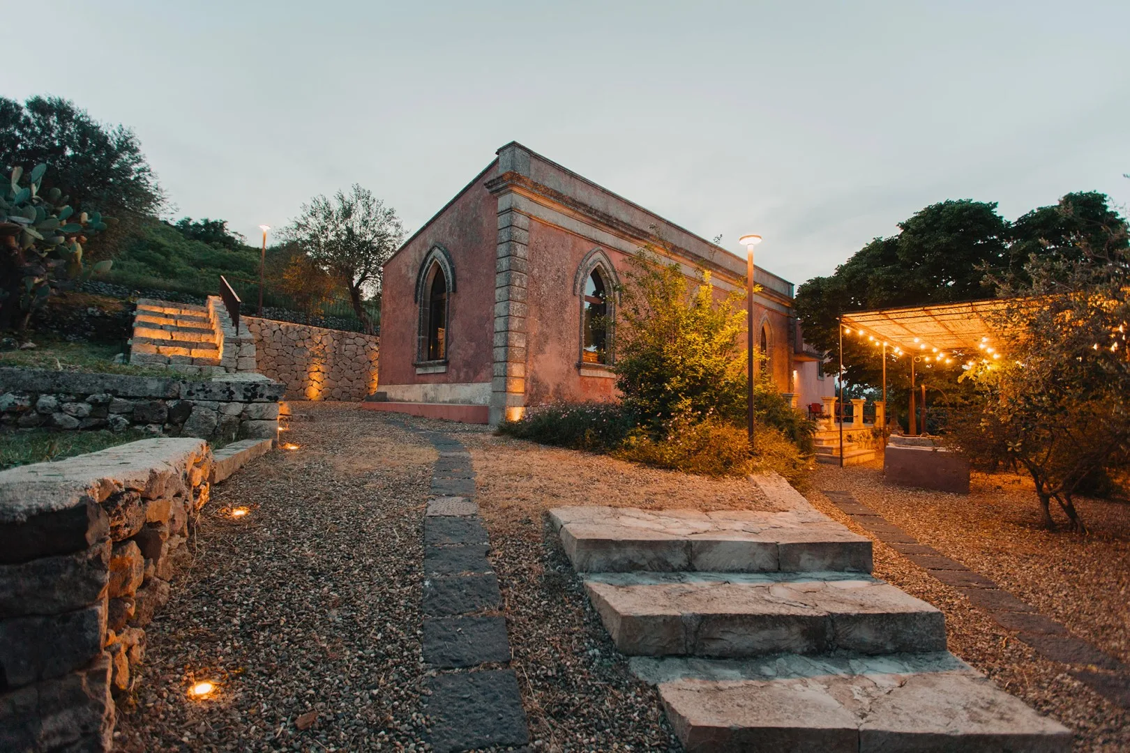Un edificio de piedra junto a un sendero de grava y una zona exterior iluminada.