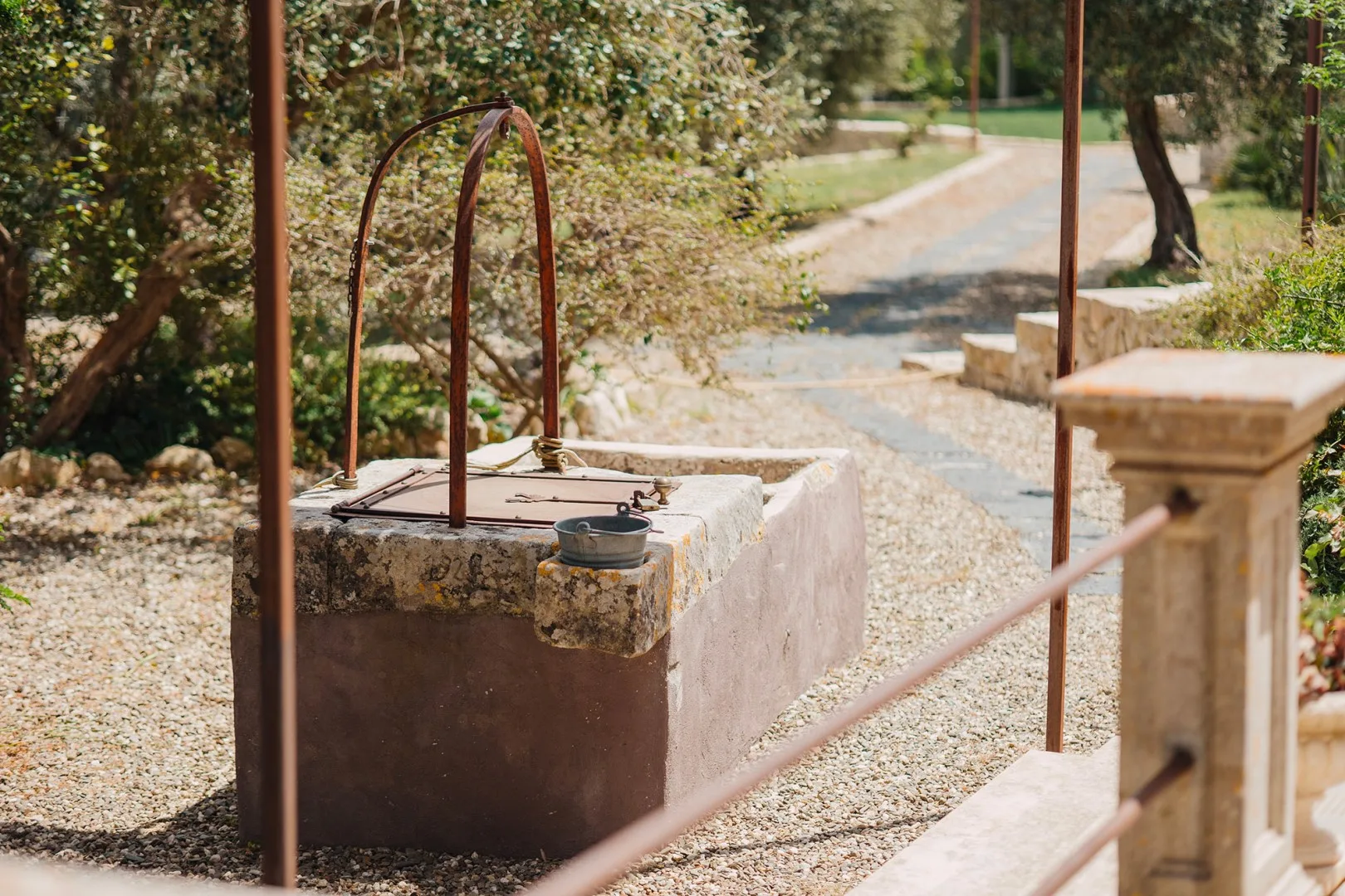 Un pozo de piedra está junto a un sendero de grava en un jardín.