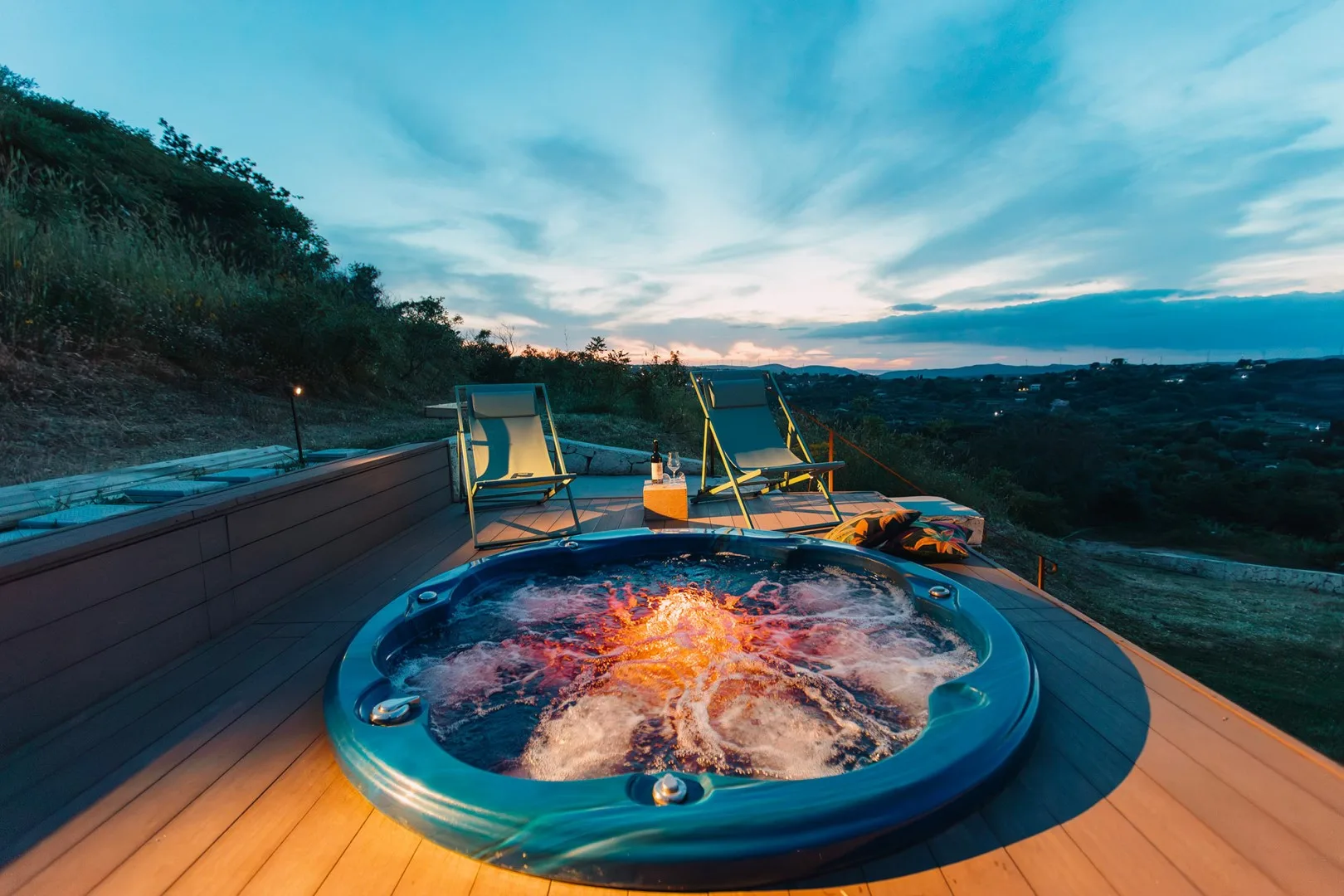 Una bañera de hidromasaje al aire libre en una terraza mira hacia un paisaje montañoso al anochecer.