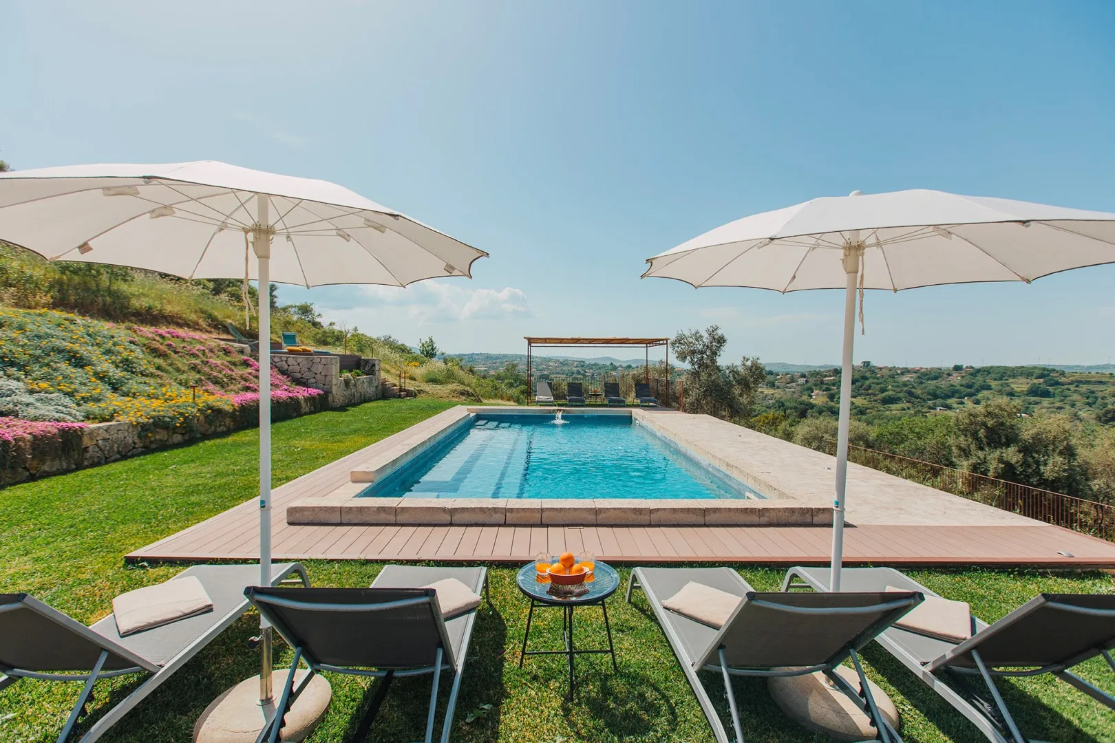 Una piscina al aire libre con asientos y sombrillas da a un paisaje verde.
