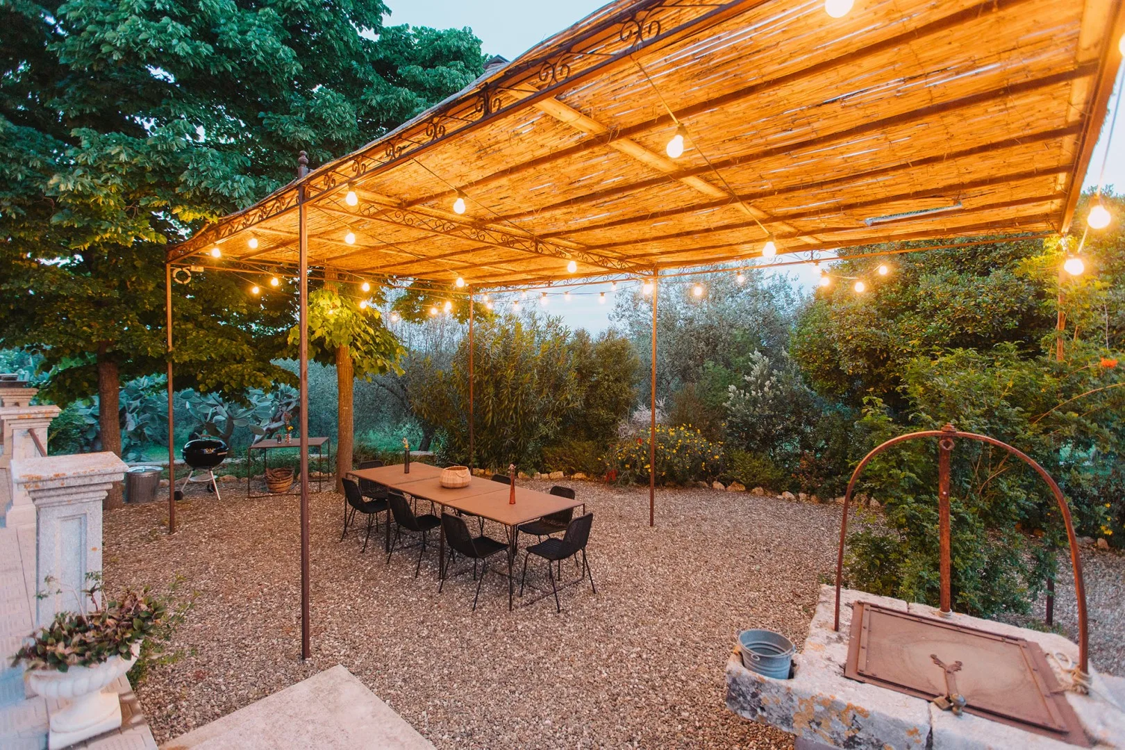 Una zona de comedor al aire libre bajo un toldo de madera con luces decorativas.