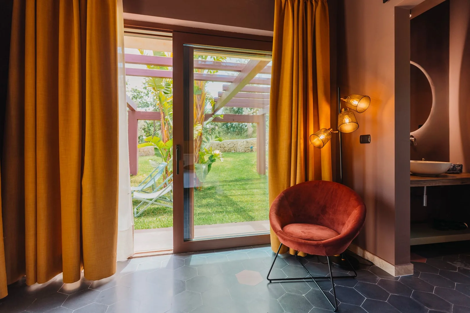 Una zona de estar con un sillón rojo junto a puertas de vidrio que dan a un jardín.