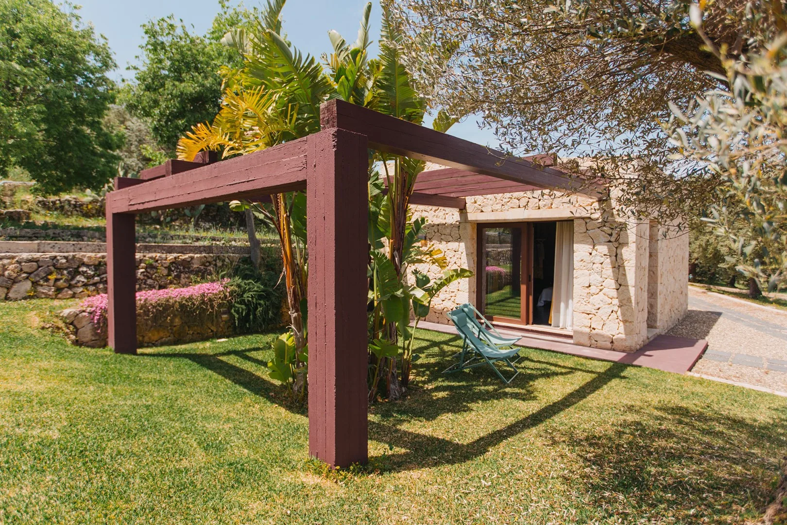 Una construcción de piedra da a un césped bajo una pérgola de madera.