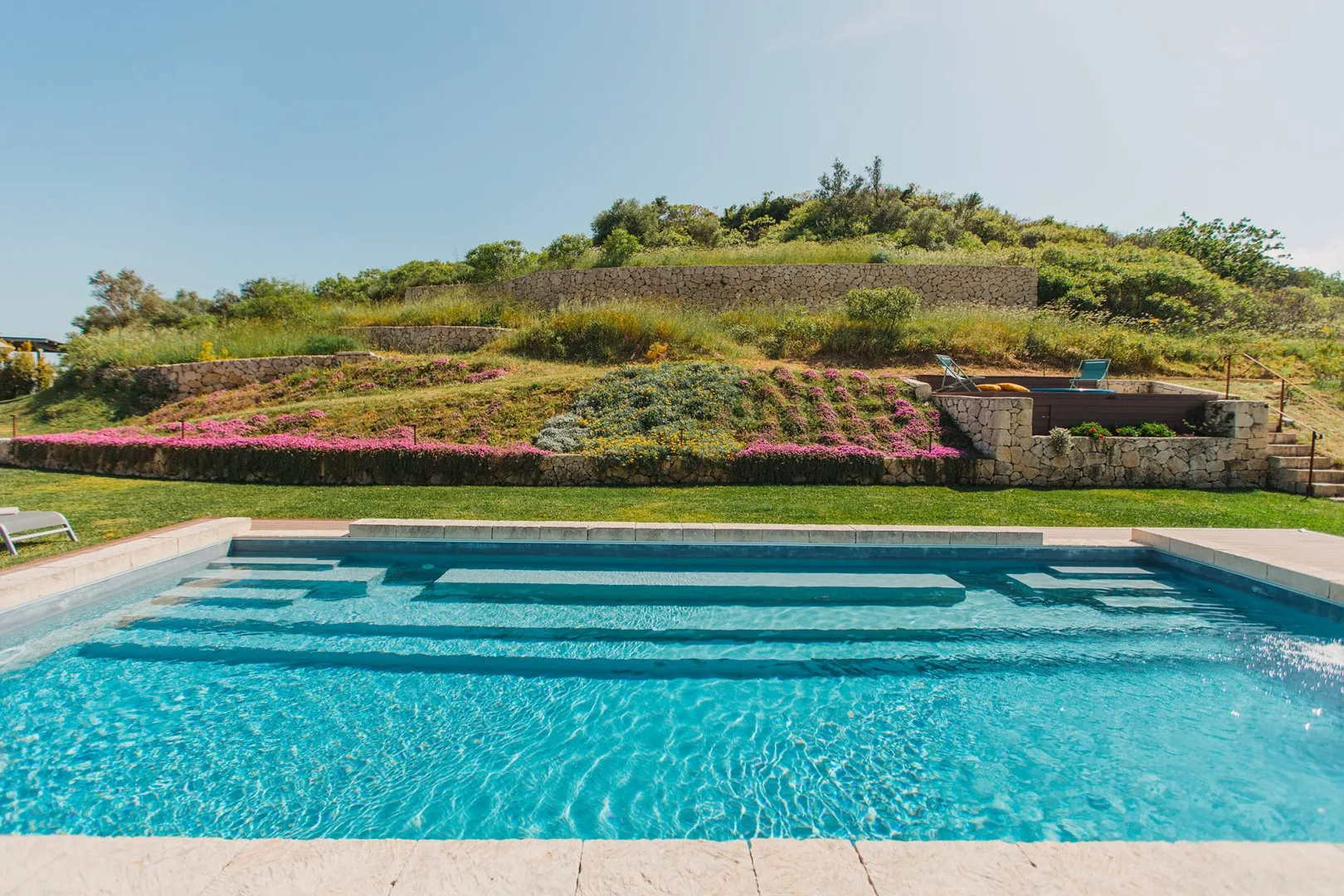 Una piscina está frente a jardines paisajísticos en un día soleado.
