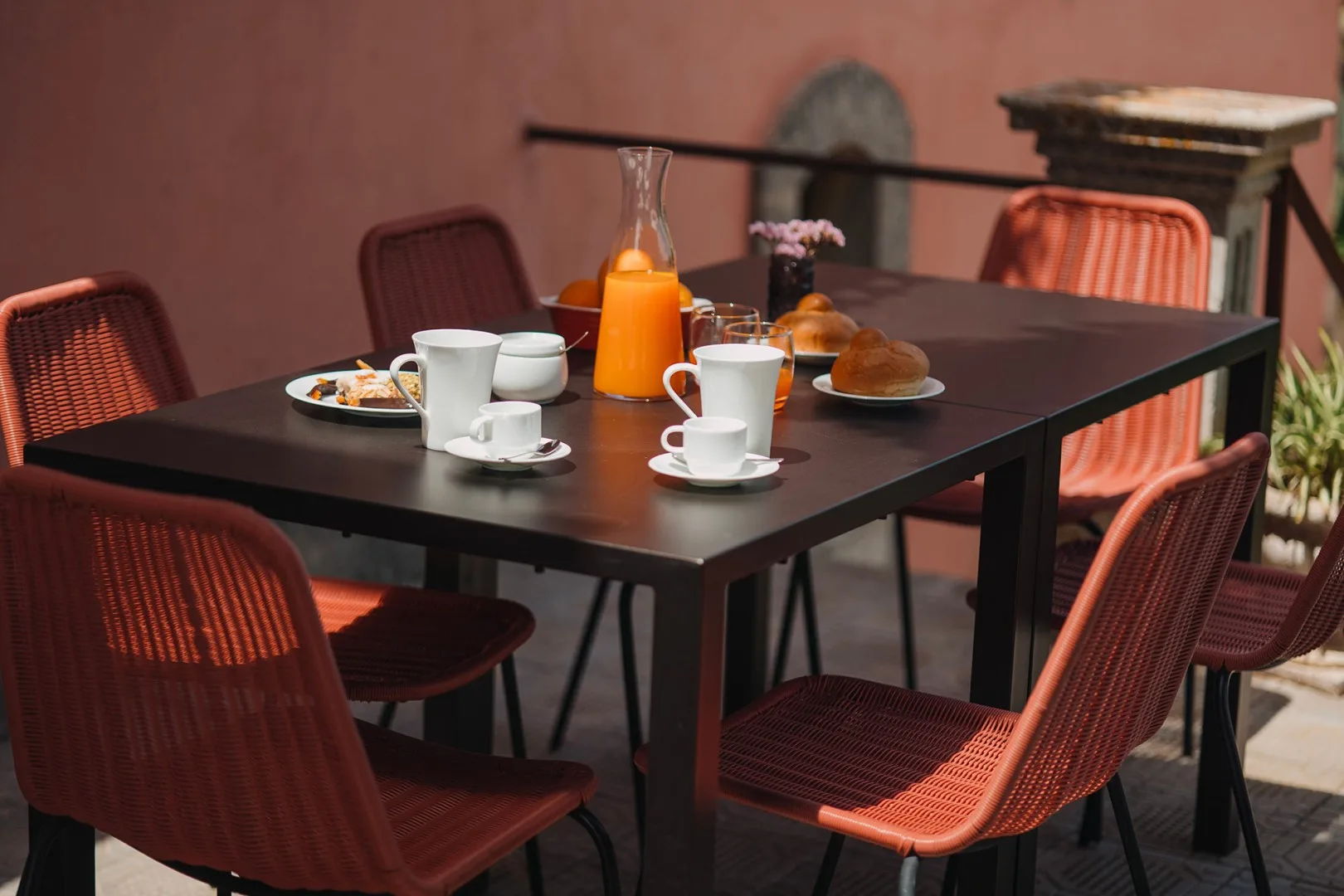 Un comedor con una mesa oscura, asientos tejidos rojos y servicio de desayuno.