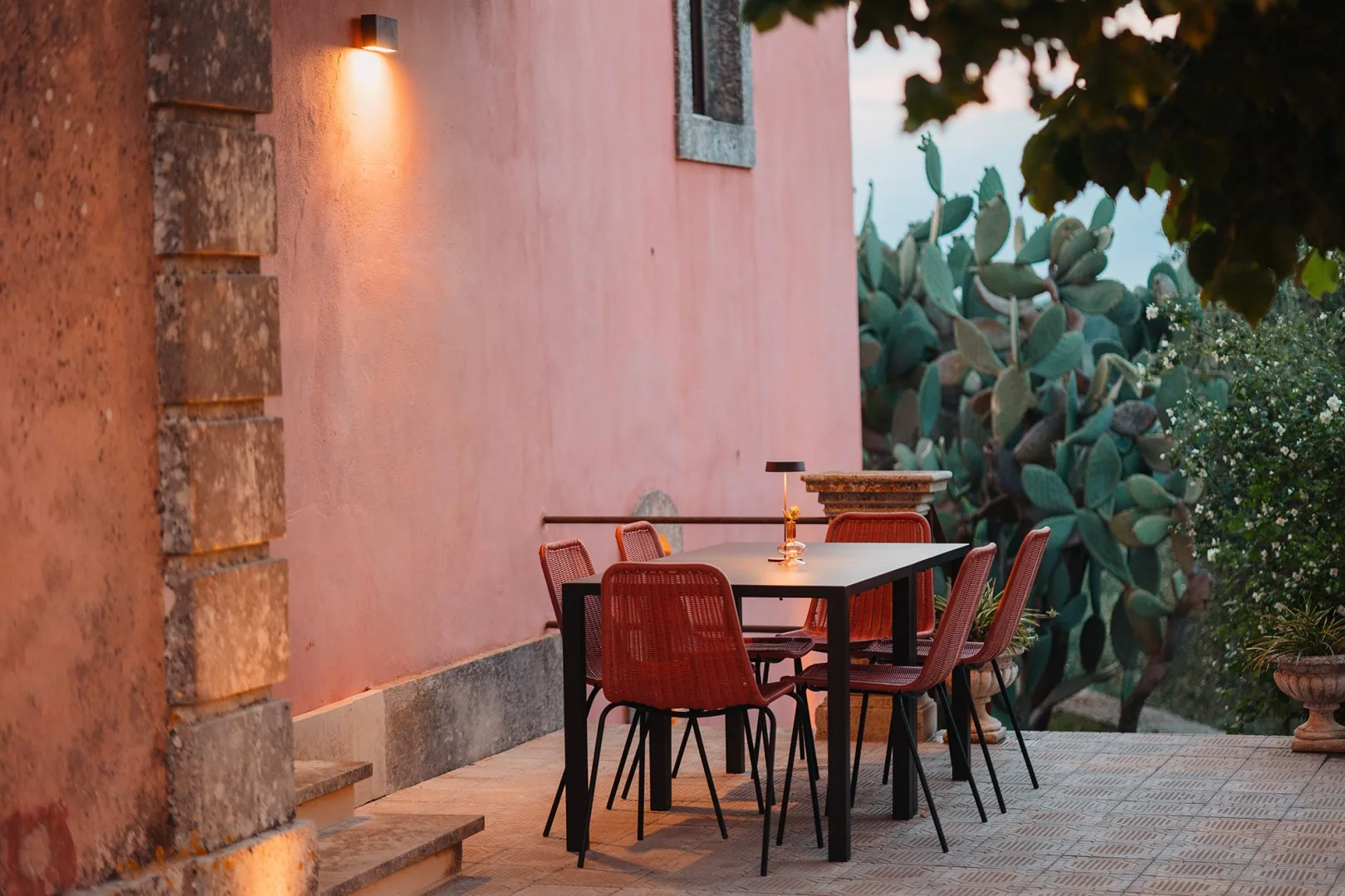 Una zona de comedor al aire libre con una mesa y asientos junto a una pared rosa.
