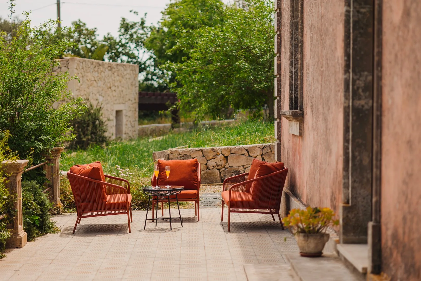 Un patio exterior con asientos rojos y una mesa pequeña junto a un muro de piedra.