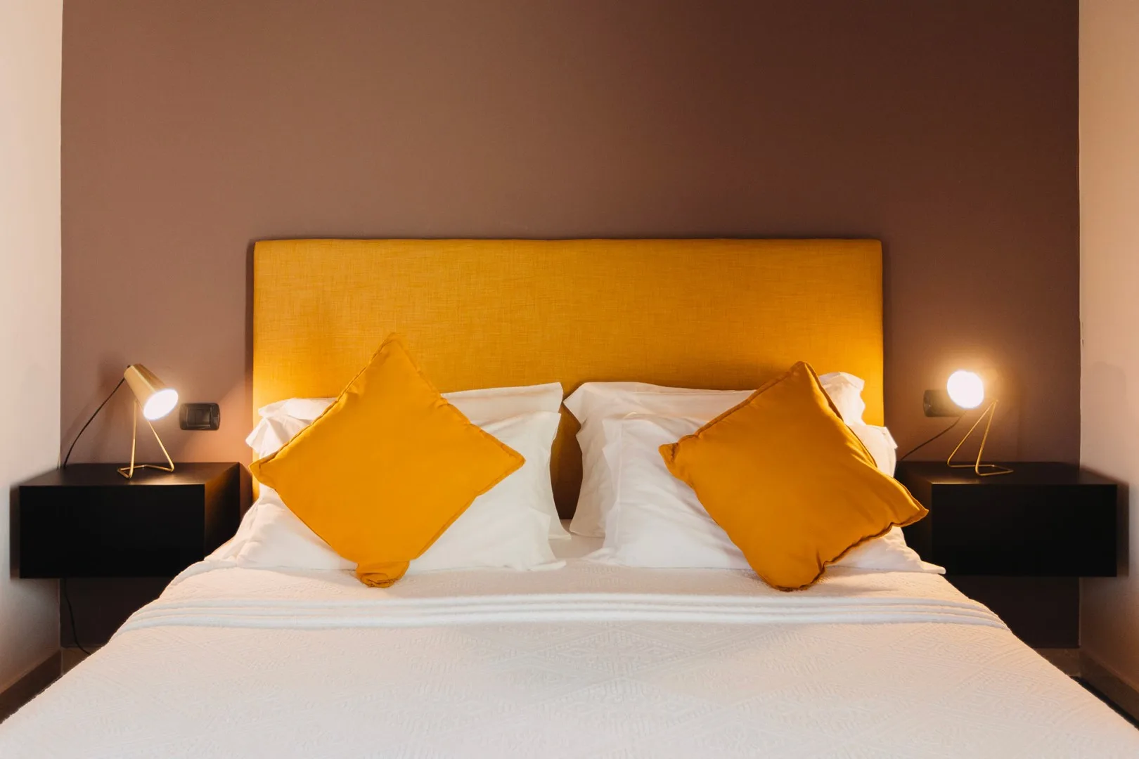 Un dormitorio con una cama, ropa de cama blanca y cojines naranjas.