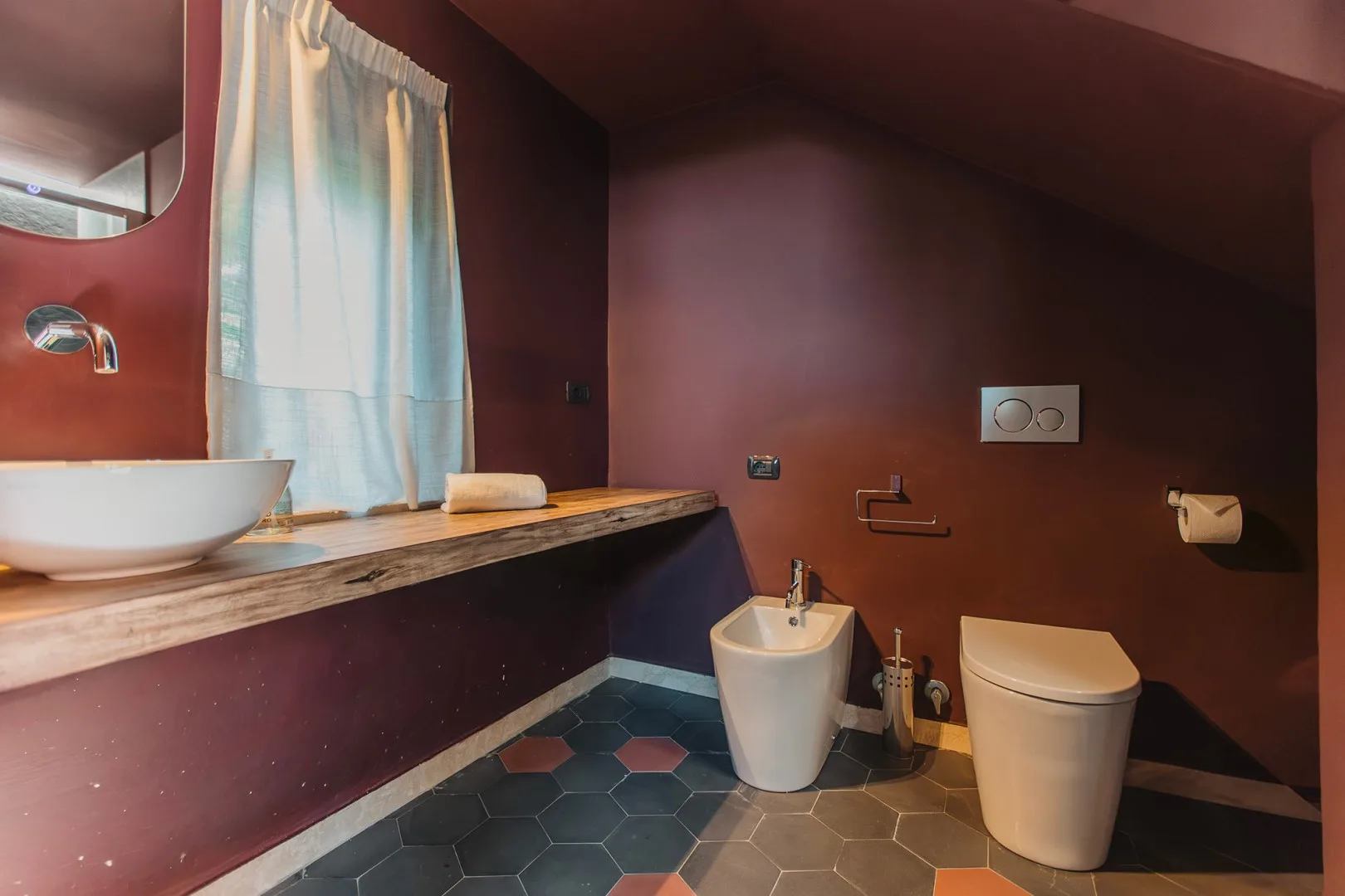 Un baño con lavabo sobre encimera, inodoro y suelo de baldosas hexagonales oscuras.