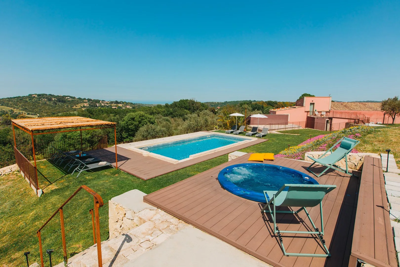 Una zona de piscina al aire libre con una piscina rectangular, una piscina redonda y asientos de descanso.