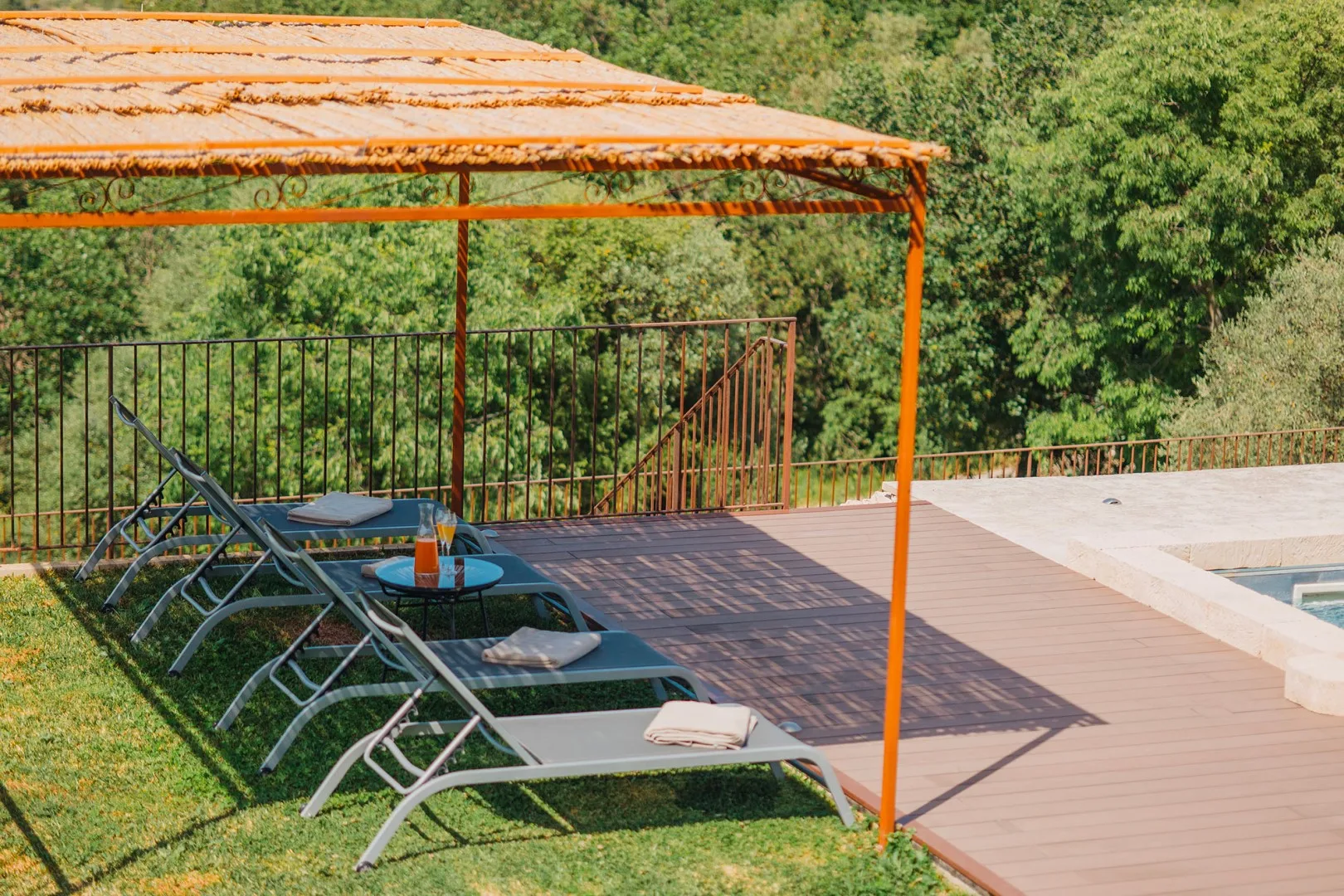 Una terraza soleada junto a la piscina tiene asientos reclinables bajo un toldo de tela.