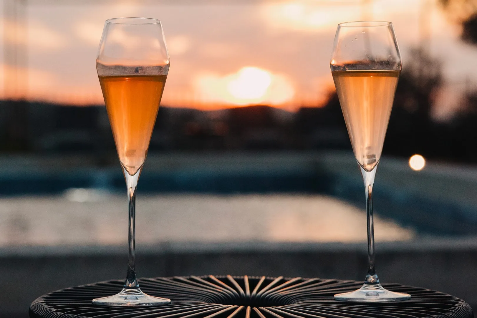 Dos copas de vino espumoso están junto a una piscina al atardecer.