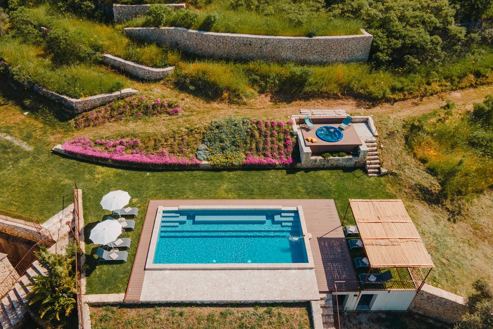 Una zona de piscina al aire libre con una piscina elevada más pequeña y jardines.