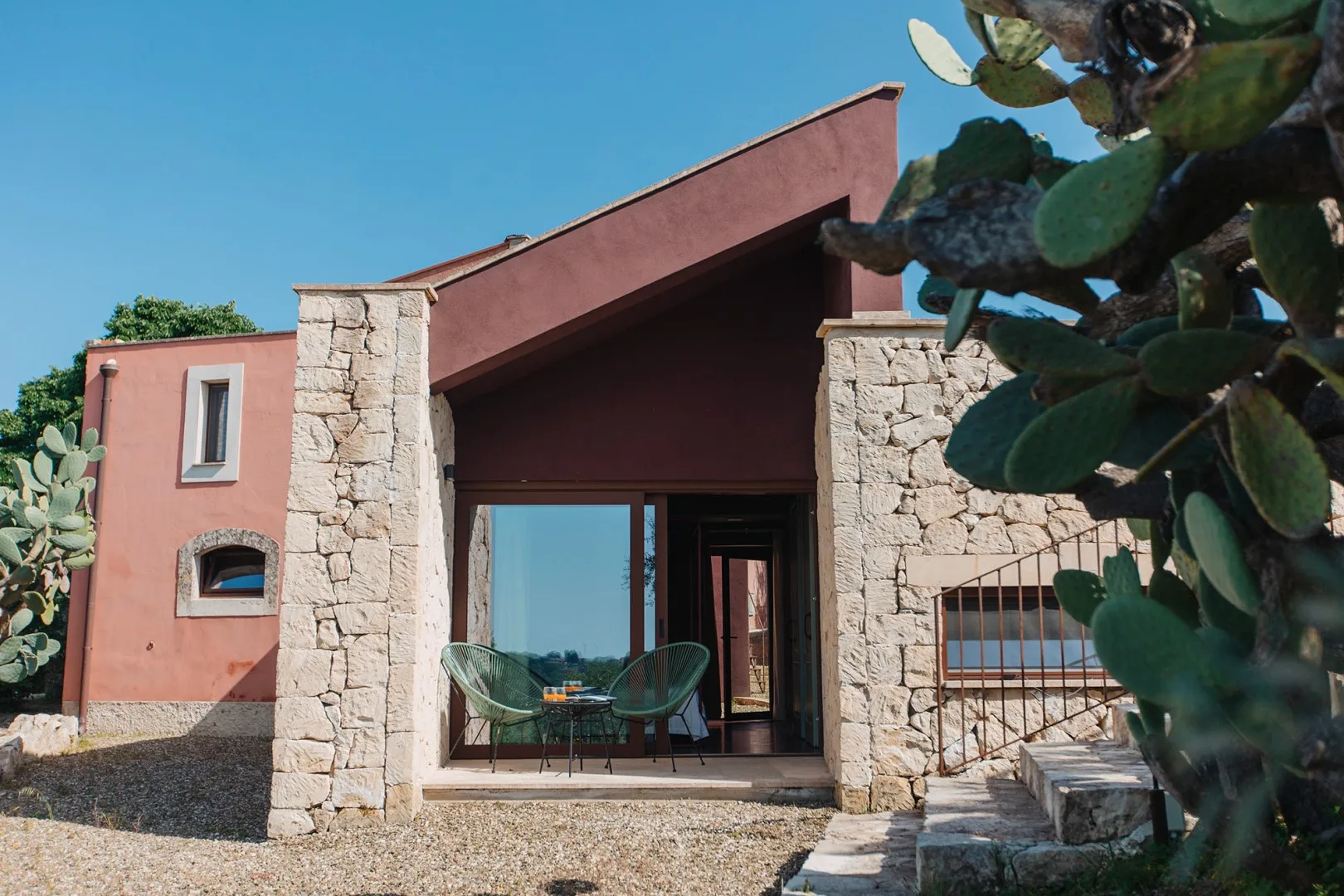 Exterior de una casa moderna con paredes de piedra, una puerta acristalada y cactus de higo chumbo.
