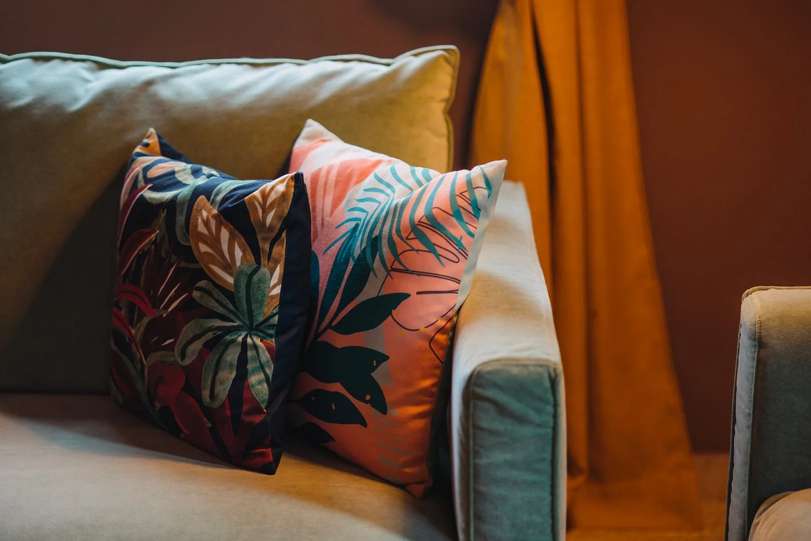 Una zona de asientos con cojines estampados de colores junto a una cortina naranja.