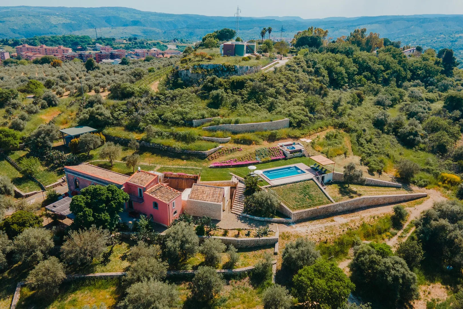 Una propiedad en una ladera con piscina está rodeada de campos verdes y árboles.