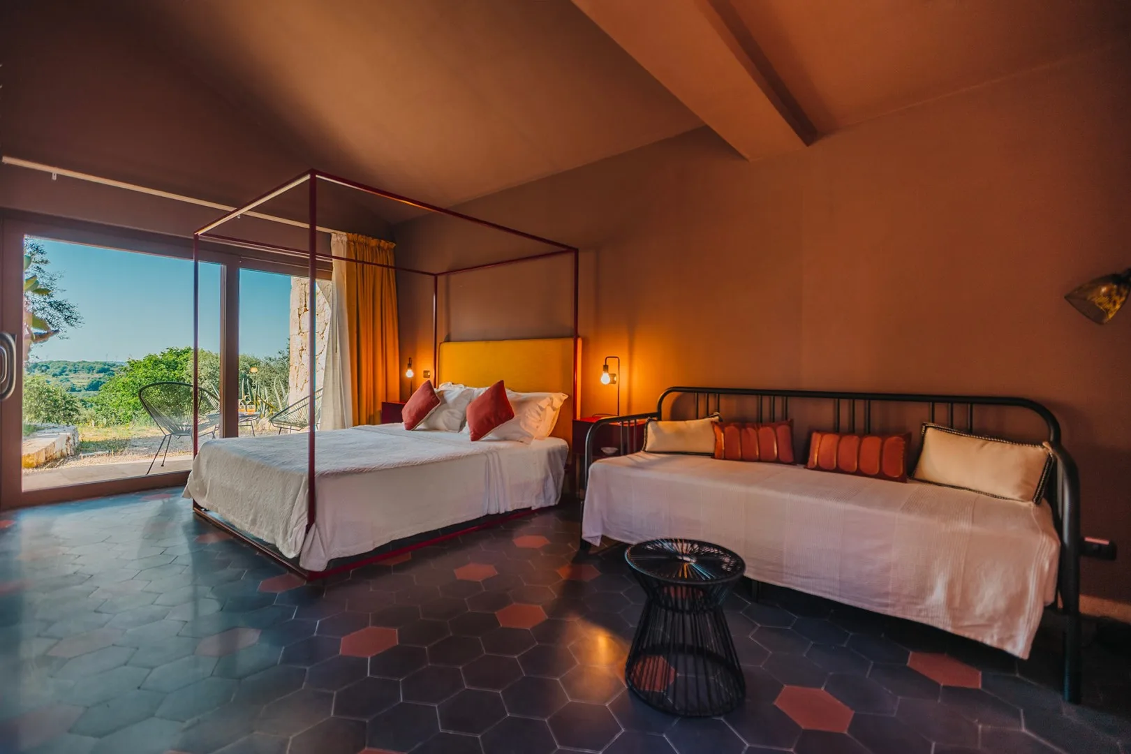 Un dormitorio con una cama grande y un diván junto a puertas de vidrio que dan a una vista.