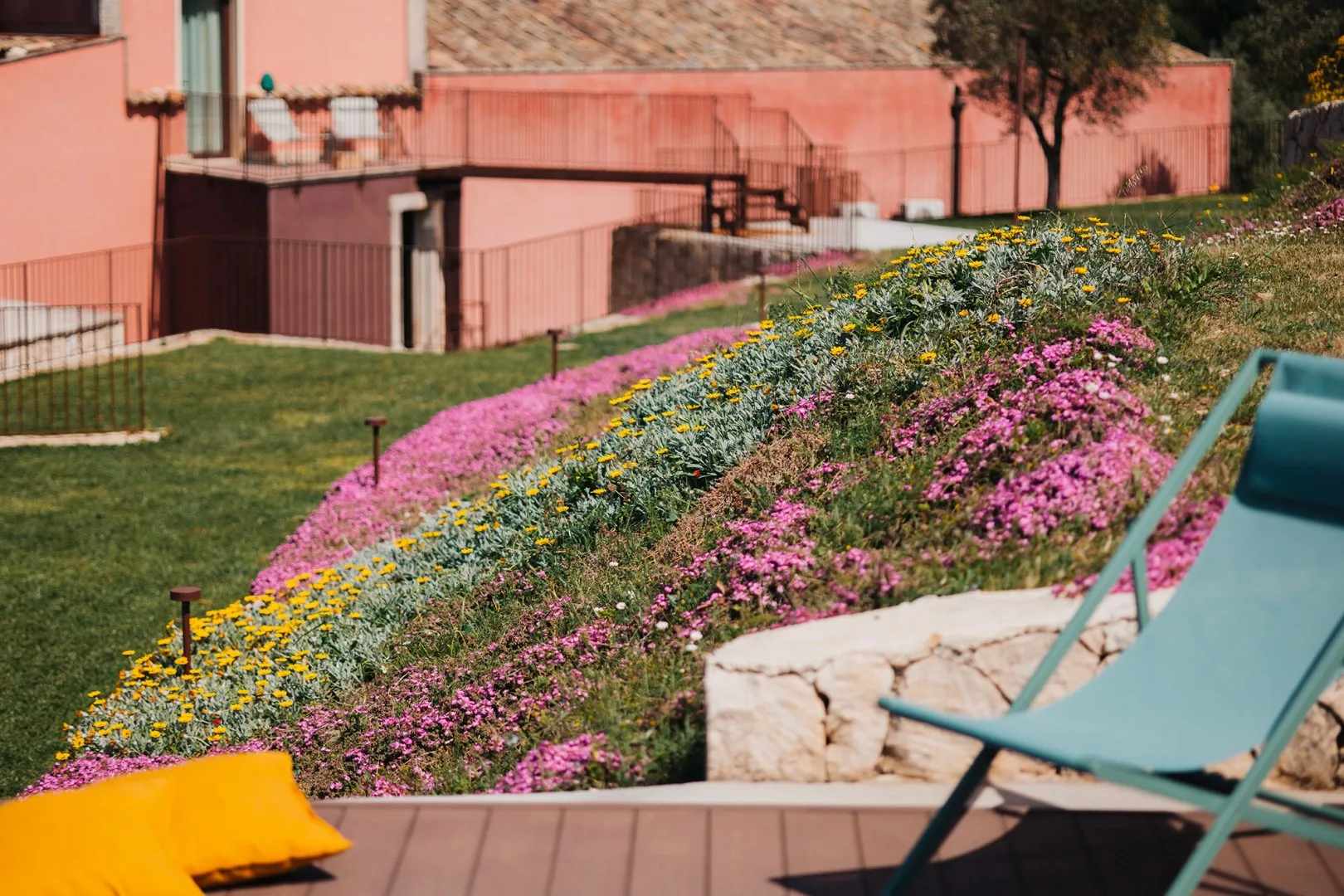 Un jardín con flores rosas y amarillas junto a asientos al aire libre.